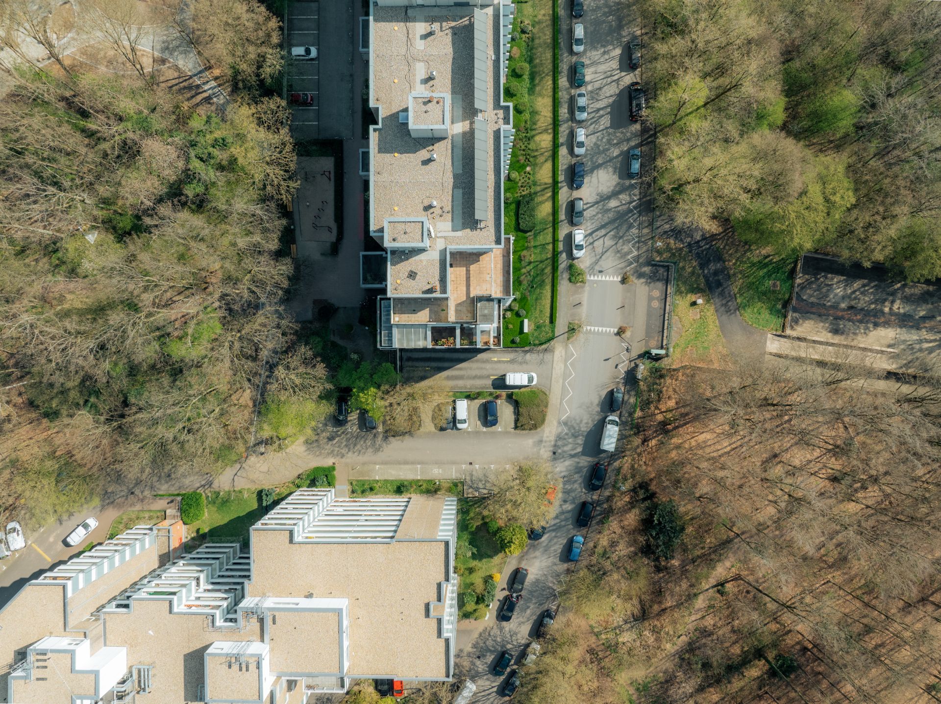 Vogelperspektive auf Wohngebäude, umgeben von Bäumen und geparkten Autos an der Straße.