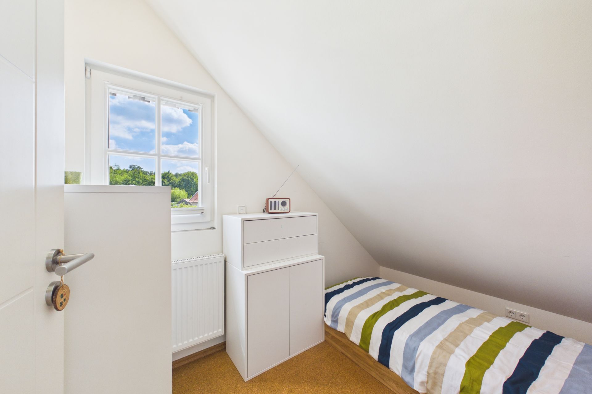 Kleines Schlafzimmer mit Einzelbett, weißem Schrank und Fenster unter einer Dachschräge.