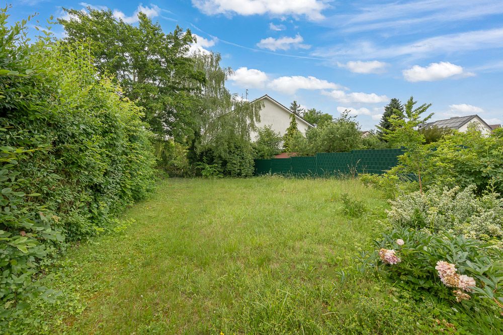 Grüner Garten mit Rasen, Büschen und Bäumen, umgeben von einem Zaun und Hecken.