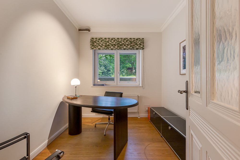 Helles Arbeitszimmer mit Schreibtisch, Stuhl und Fenster mit Blick ins Grüne.