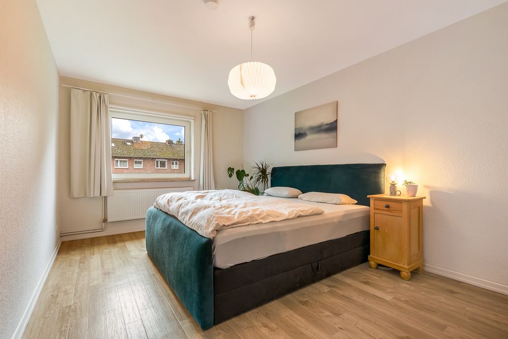 Helles Schlafzimmer mit Doppelbett, Nachttisch, Fenster, Bild an der Wand und Holzfußboden.
