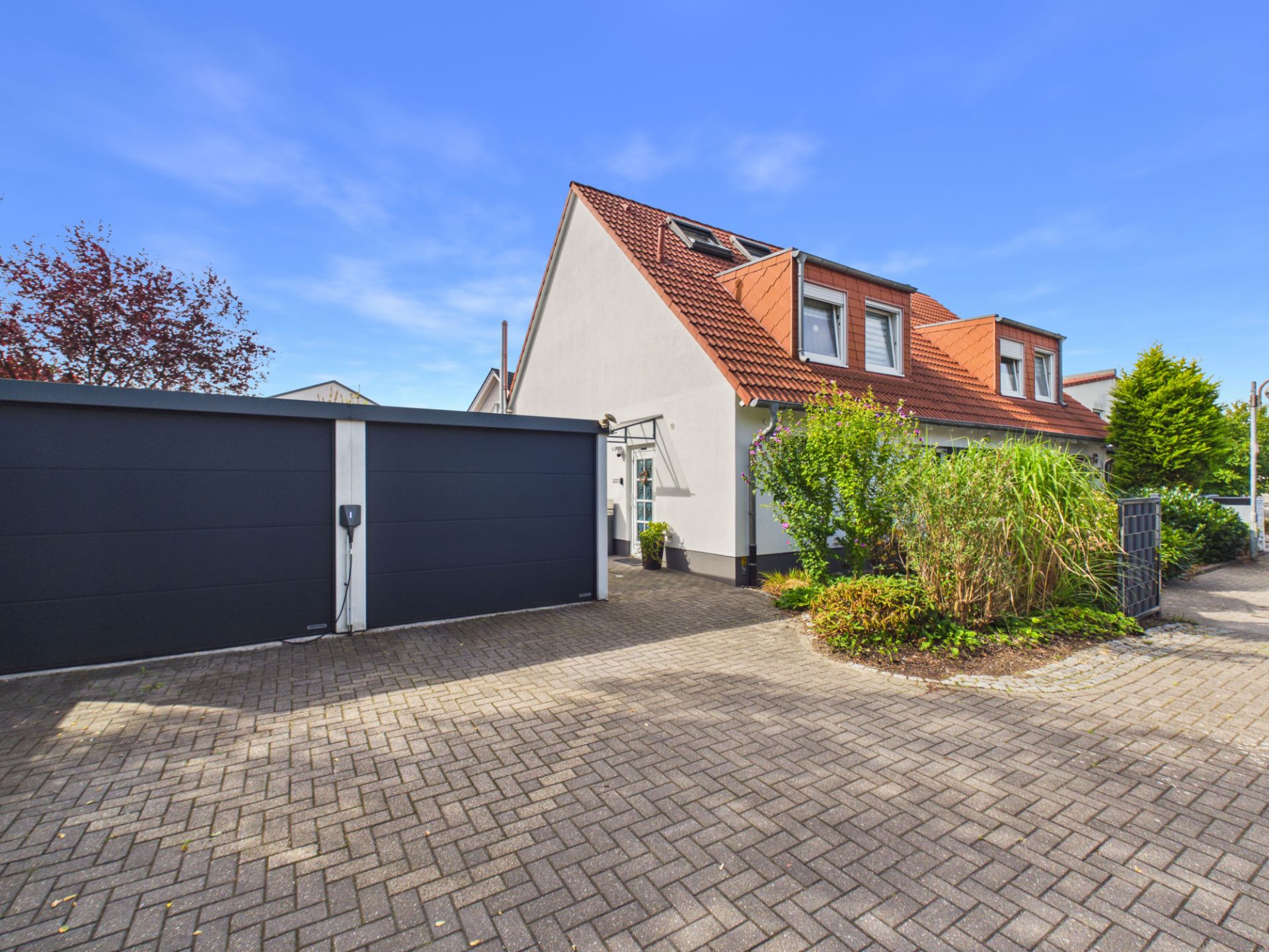 Helles Wohnhaus mit rotem Dach, großer Garage und gepflasterter Einfahrt.