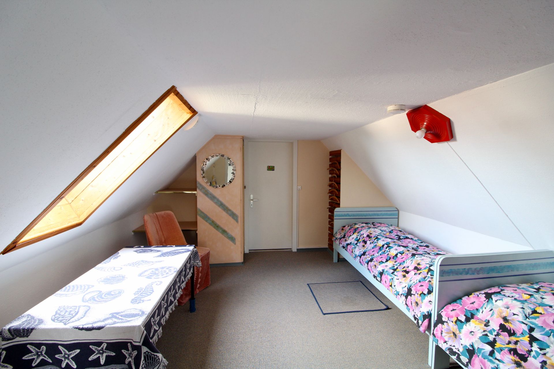 Dachzimmer mit zwei Einzelbetten, Schreibtisch, Stuhl und Dachfenster.