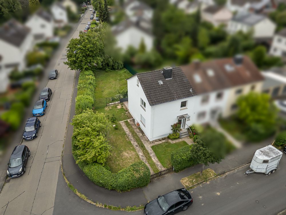 Zweistöckiges Wohnhaus mit Garten an einer Straßenecke, mehrere parkende Autos sichtbar.
