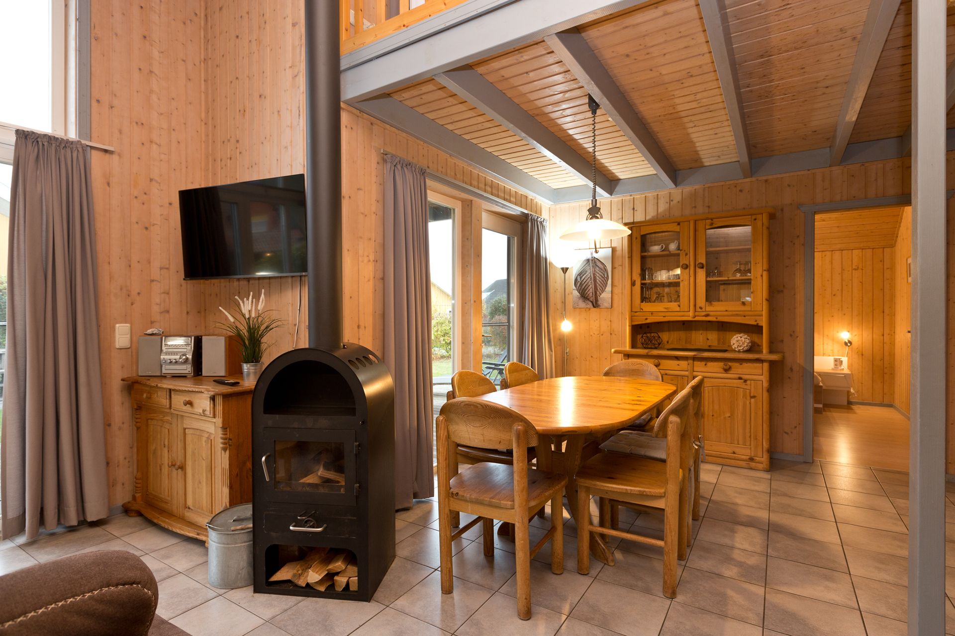Essbereich mit Holztisch, Stühlen, Kaminofen und großen Fenstern in einem Wohnzimmer aus Holz.
