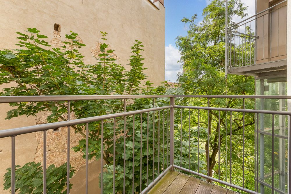 Balkon mit Metallgeländer und Blick auf grüne Bäume und benachbarte Hauswand.