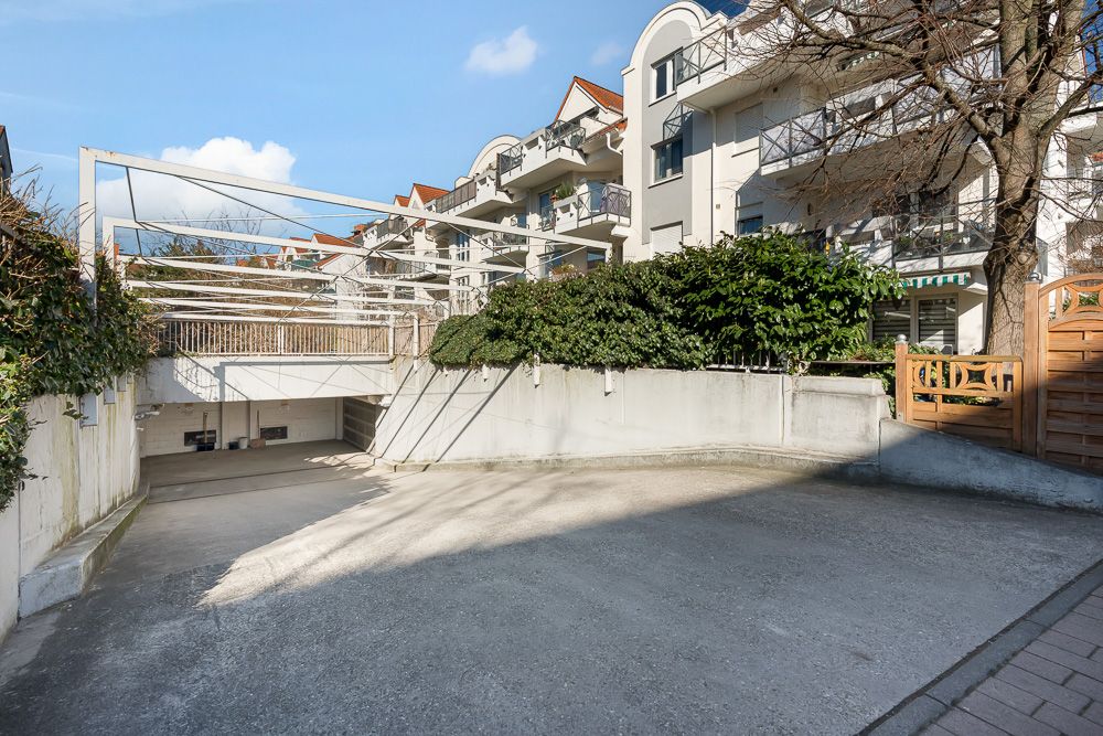 Einfahrt zu einer Tiefgarage vor einem Wohnhaus mit Balkonen und Grünpflanzen.