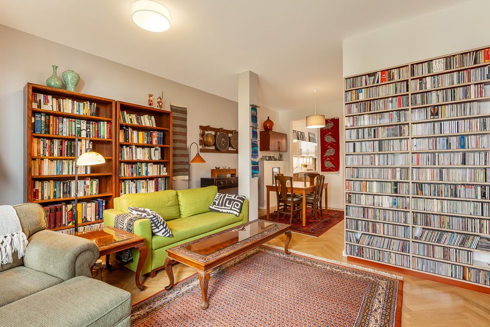 Wohnzimmer mit Bücherregalen, grüner Couch, vielen CDs und Esstisch im Hintergrund.