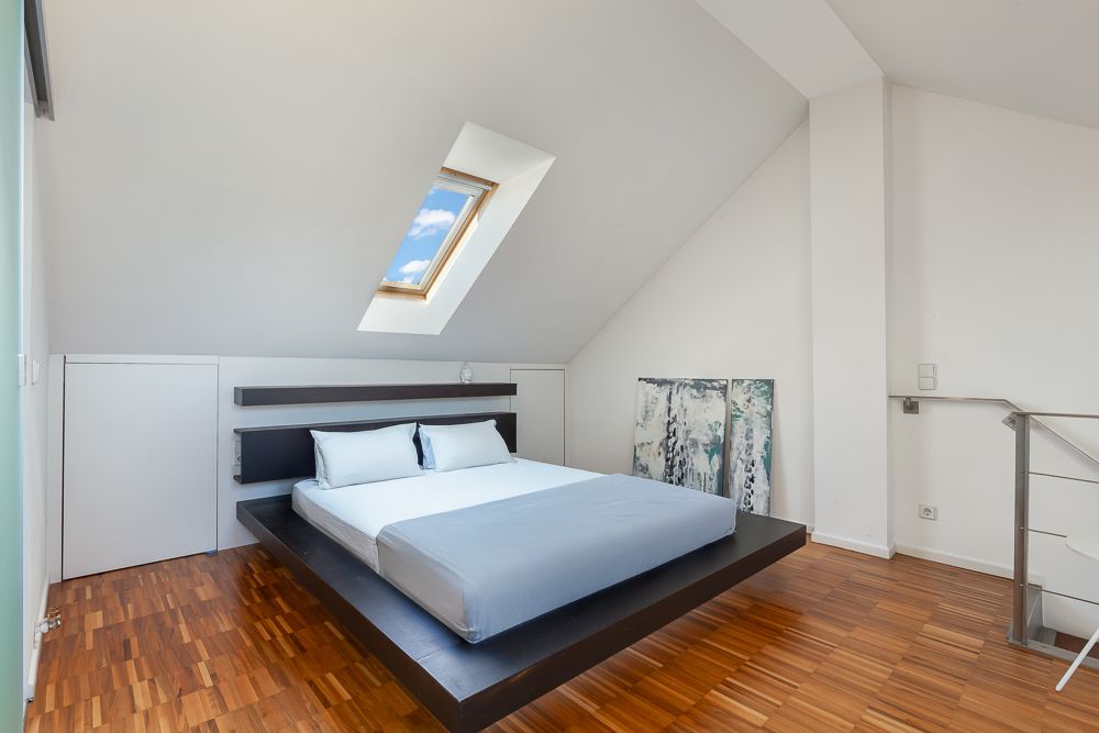 Modernes Schlafzimmer mit Doppelbett unter Dachschräge und Dachfenster, Holzfußboden.