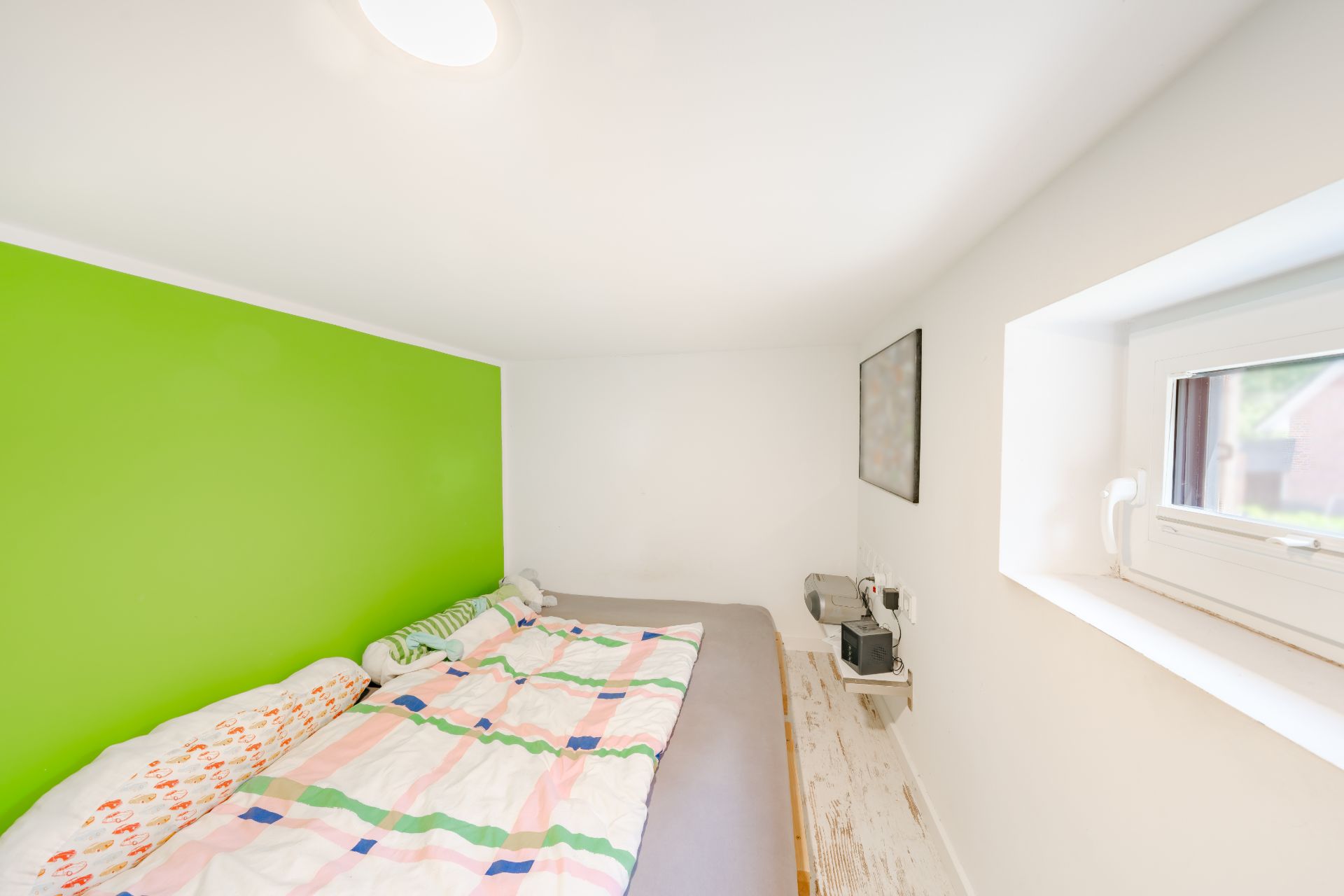 Helles Schlafzimmer mit grün gestrichener Wand, Doppelbett und Fenster.