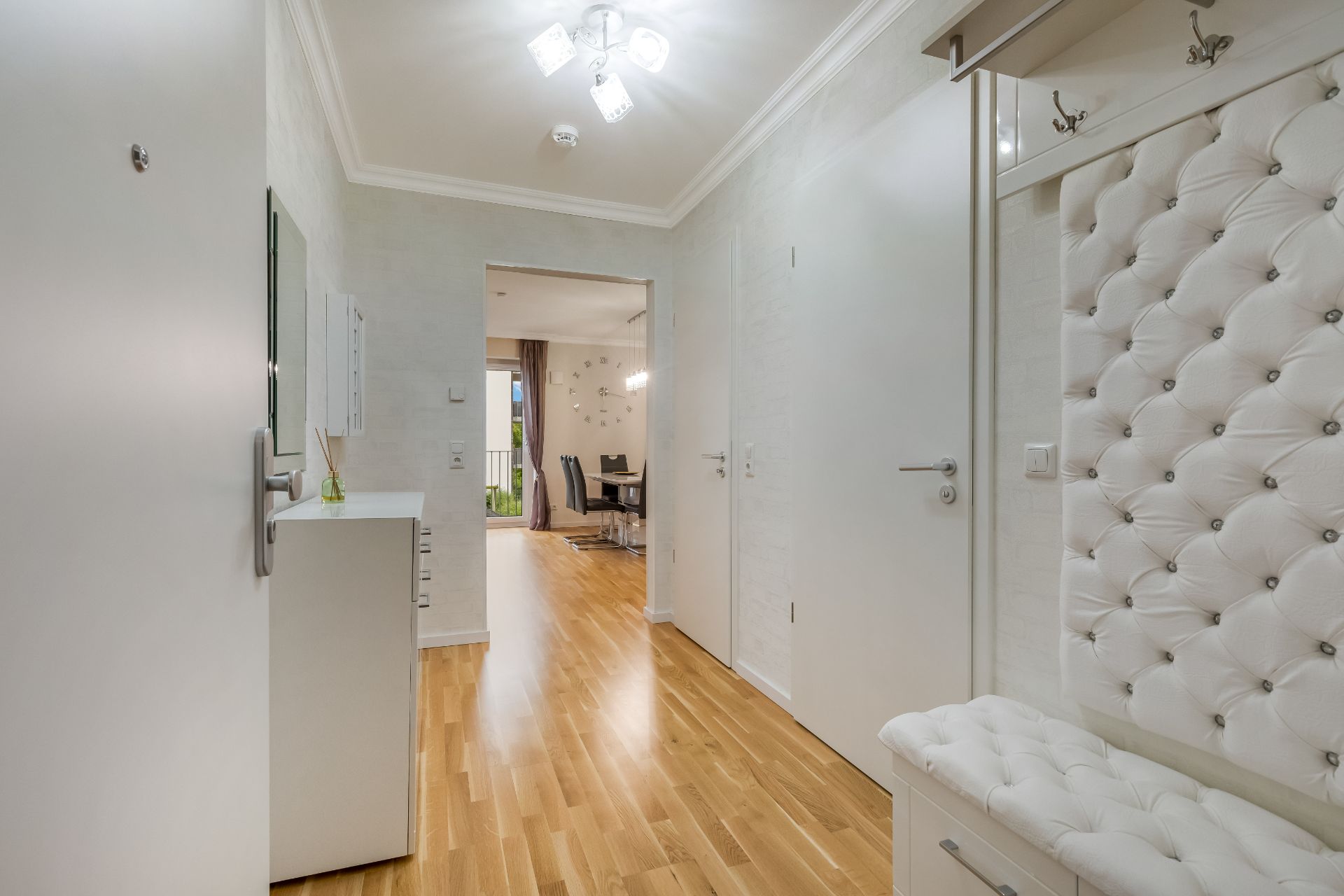 Heller Flur mit Parkettboden, weißem Schuhschrank und gepolsterter Sitzbank, Blick ins Esszimmer.
