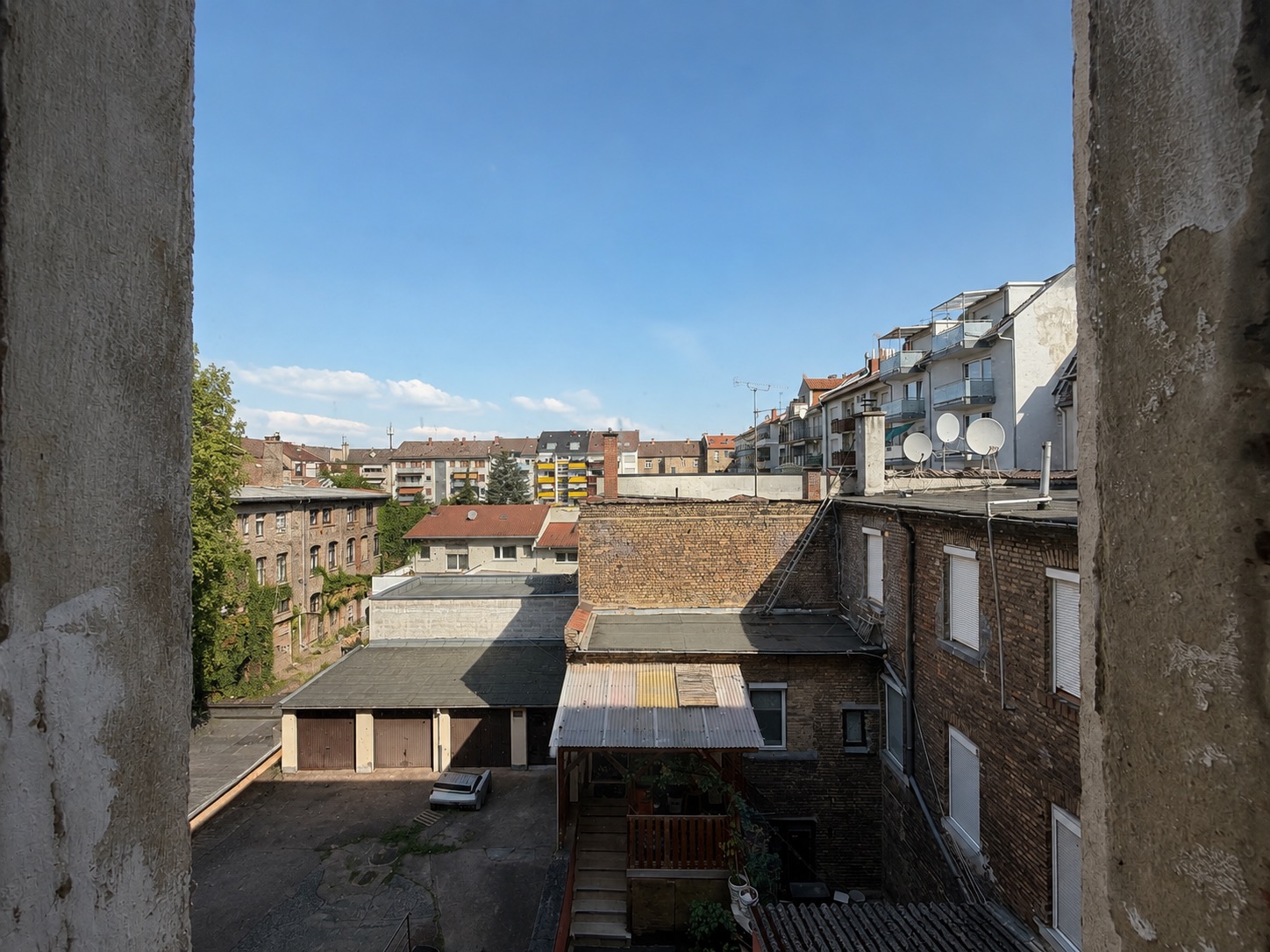 Blick aus einem Fenster auf einen Hinterhof mit Wohngebäuden und Garagen bei Tageslicht.