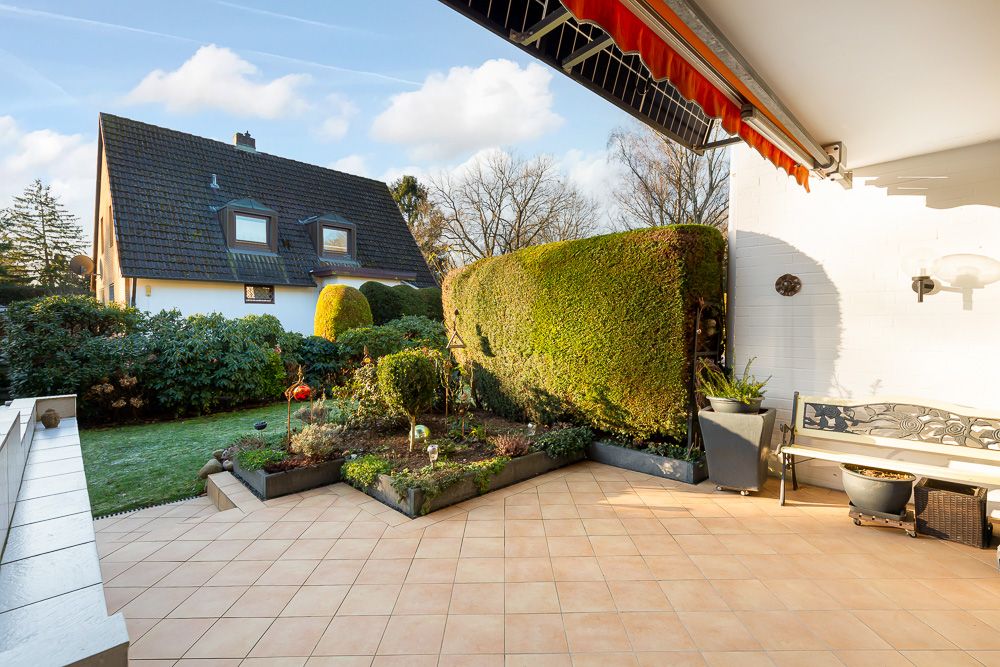 Große Terrasse mit Fliesenboden, Gartenbeet, Bank und Blick auf ein Nachbarhaus.