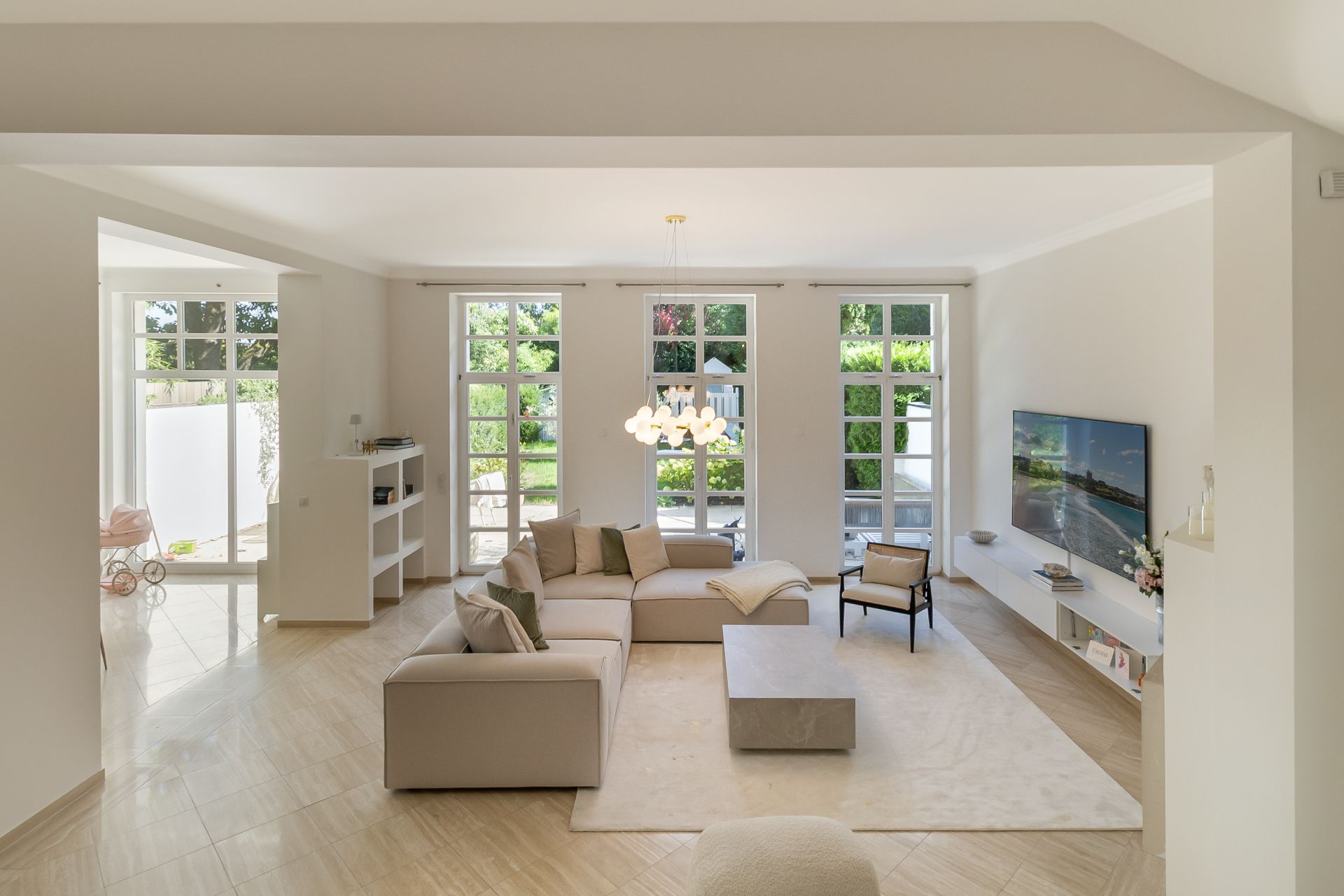 Helles Wohnzimmer mit Ecksofa, Couchtisch, Teppich und großem Fernseher vor bodentiefen Fenstern.