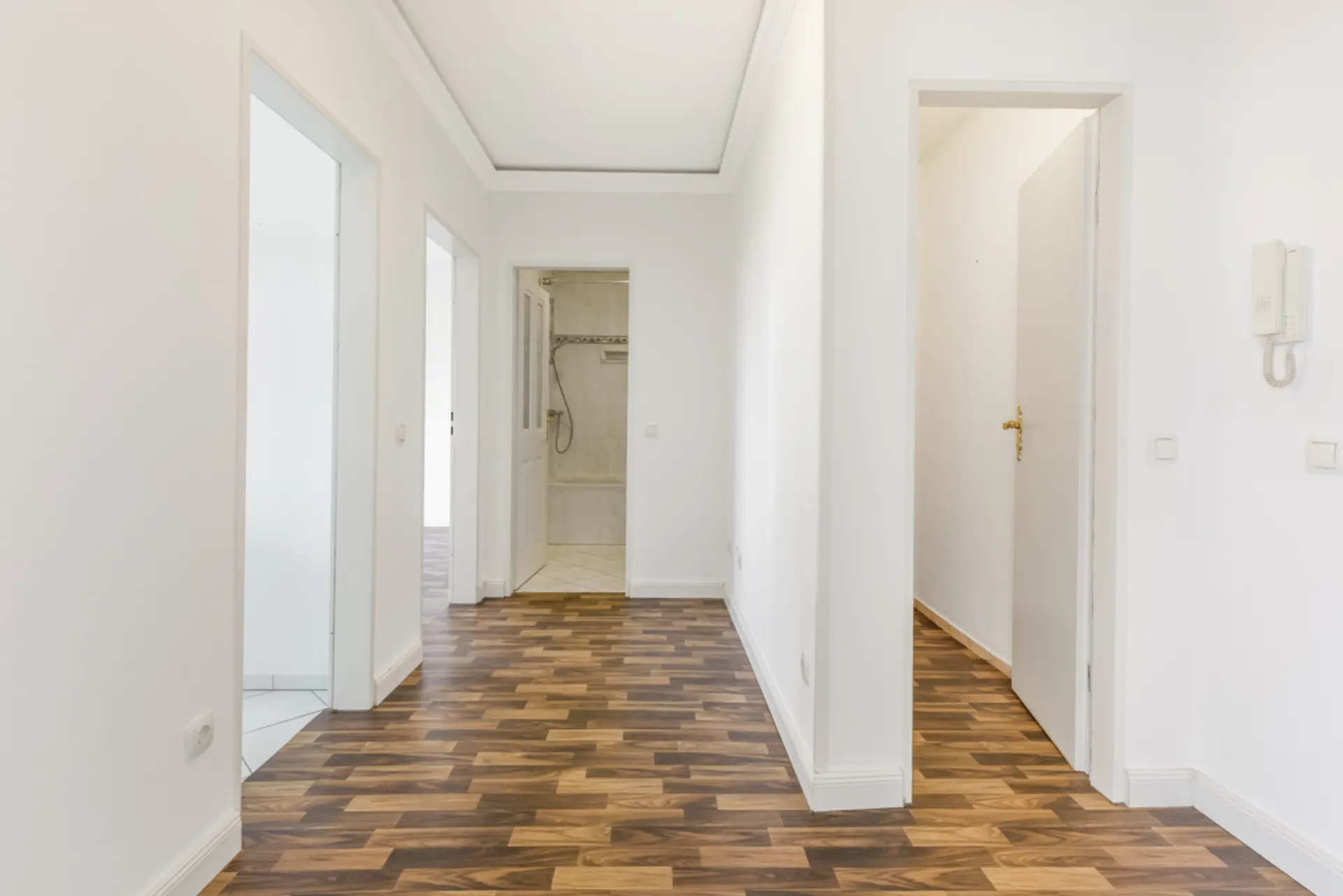 Flur mit Holzboden und mehreren offenen Türen, weiße Wände, Sicht auf Badezimmer.