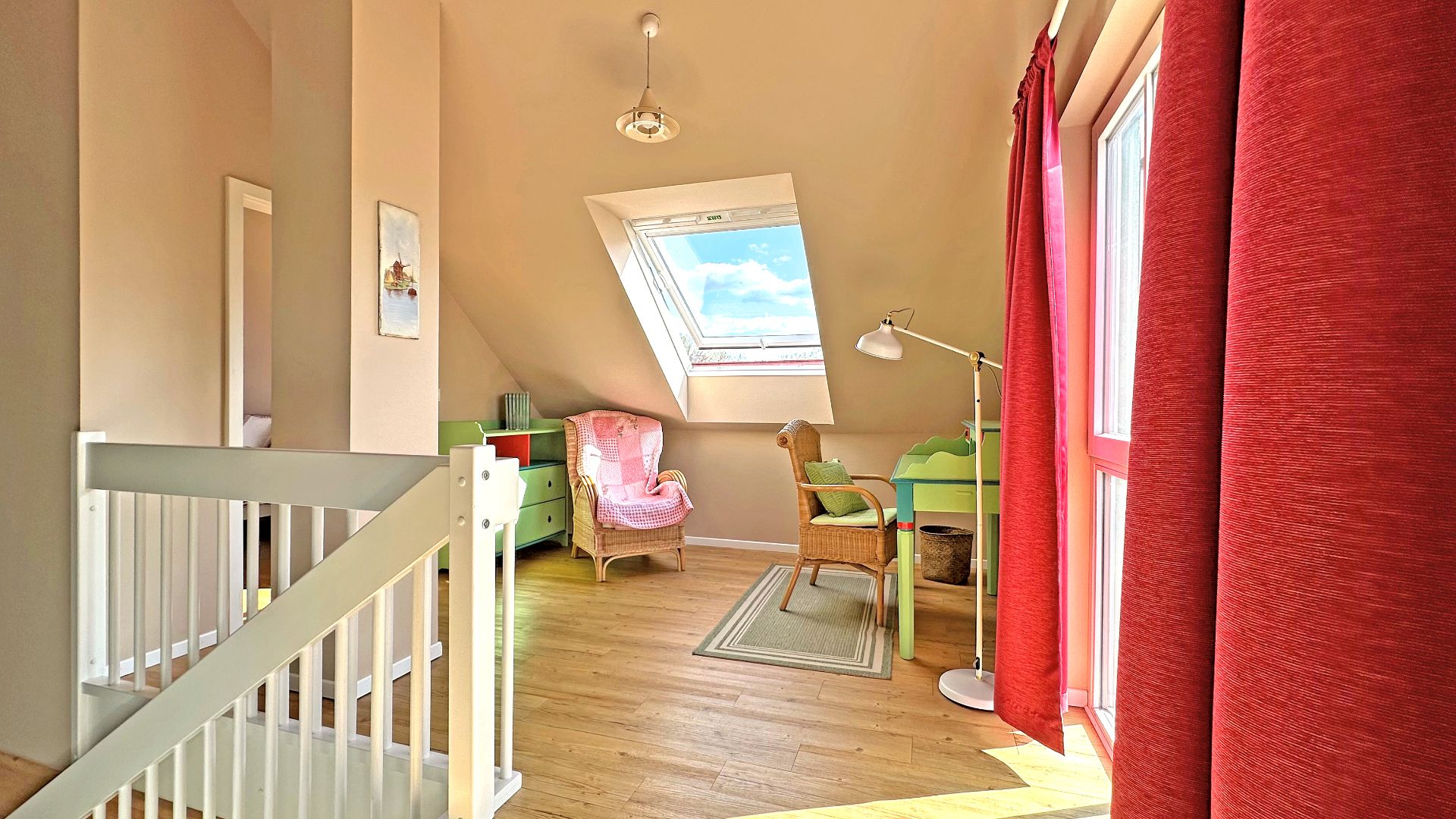 Helles Zimmer mit Dachfenster, Schreibtisch, Sessel und Holzfußboden neben einer Treppe.