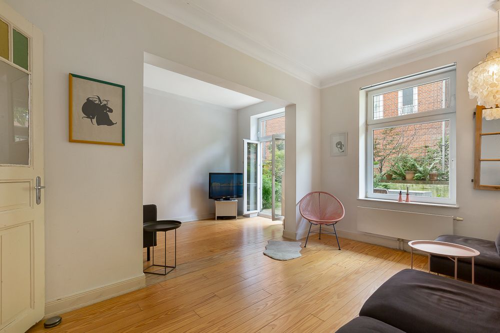 Helles Wohnzimmer mit Holzboden, Sofa, Stuhl, Fernseher und Blick auf den Garten.