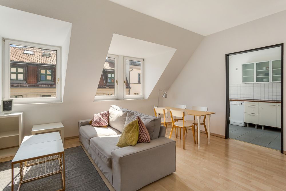 Helles Wohnzimmer mit Sofa, Esstisch, drei Fenstern und Durchgang zur Küche.
