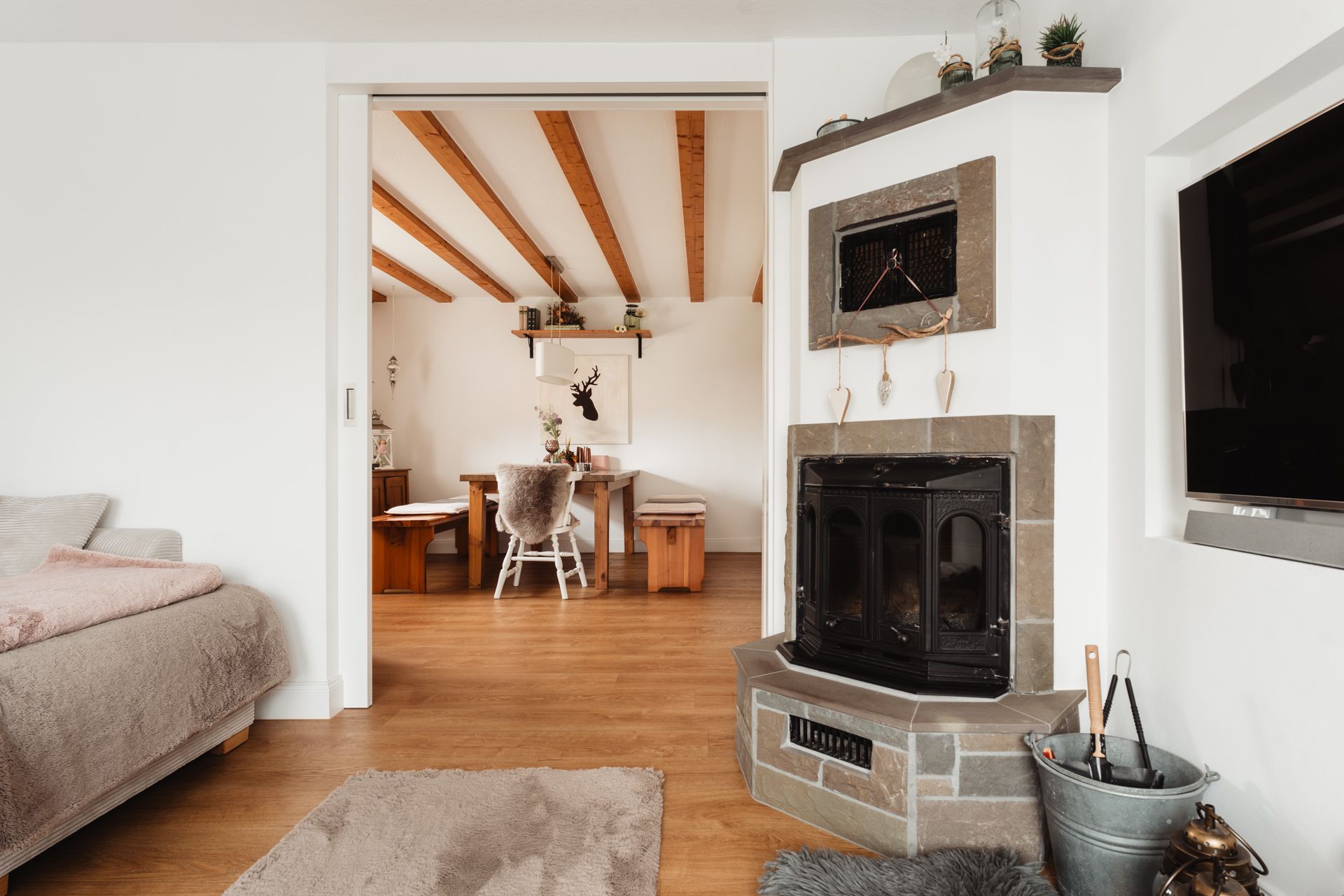 Gemütliches Wohnzimmer mit Eckkamin, Sofa, Teppich und Blick auf Essbereich mit Holzbalkendecke.