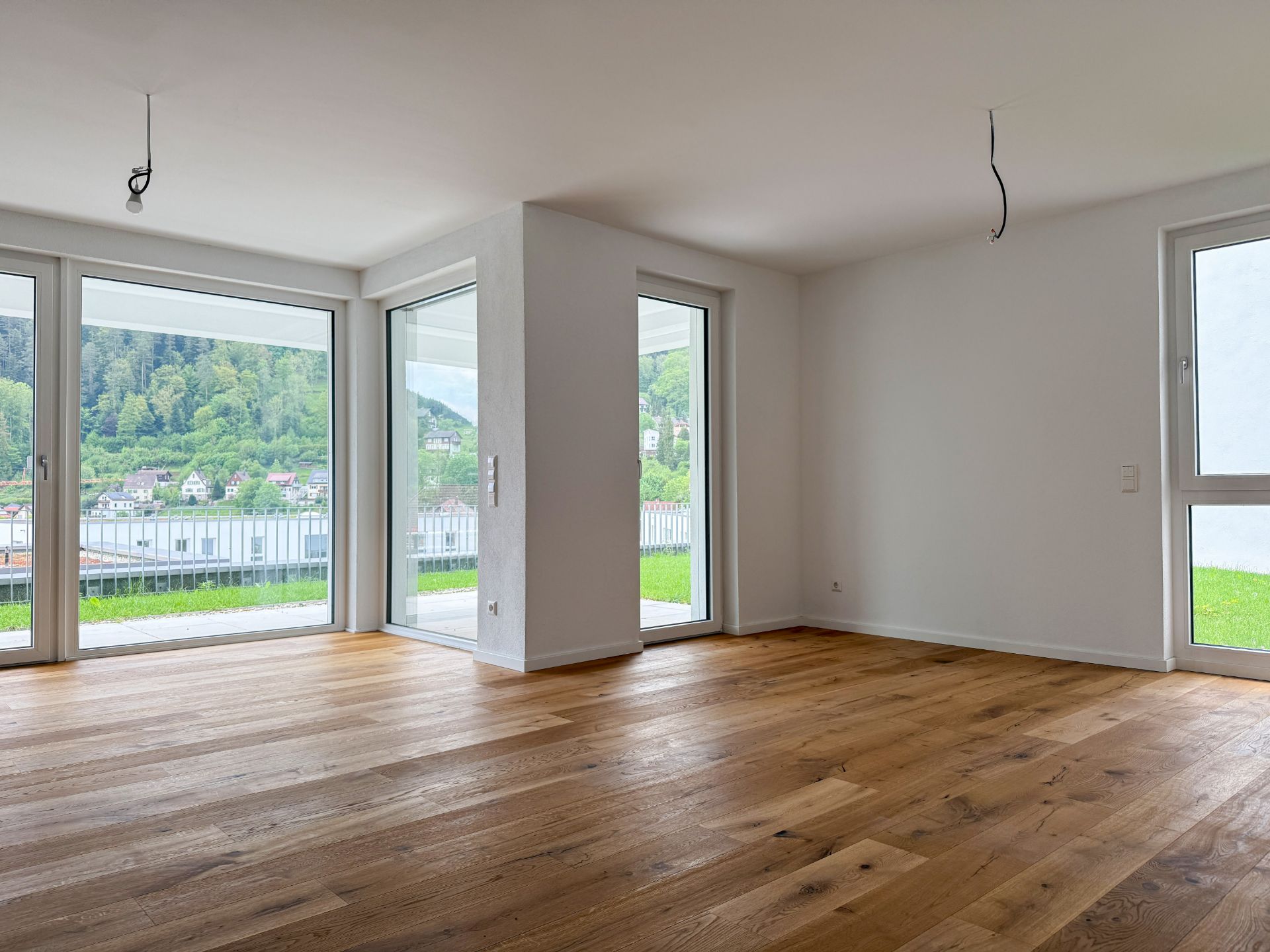 Helles Wohnzimmer mit Holzboden, großen Fenstern und Blick ins Grüne.
