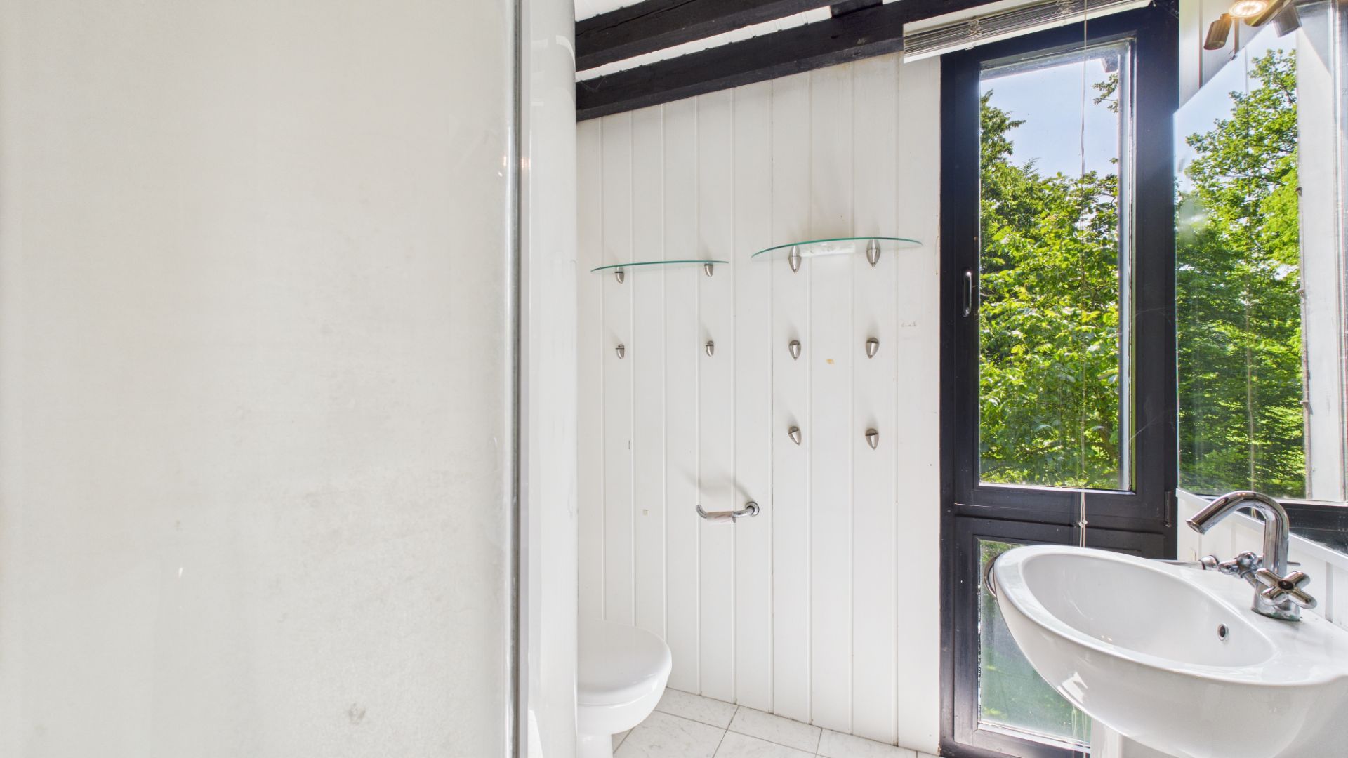 Helles Bad mit Waschbecken, WC, Wandhaken und Fenster mit Blick ins Grüne.