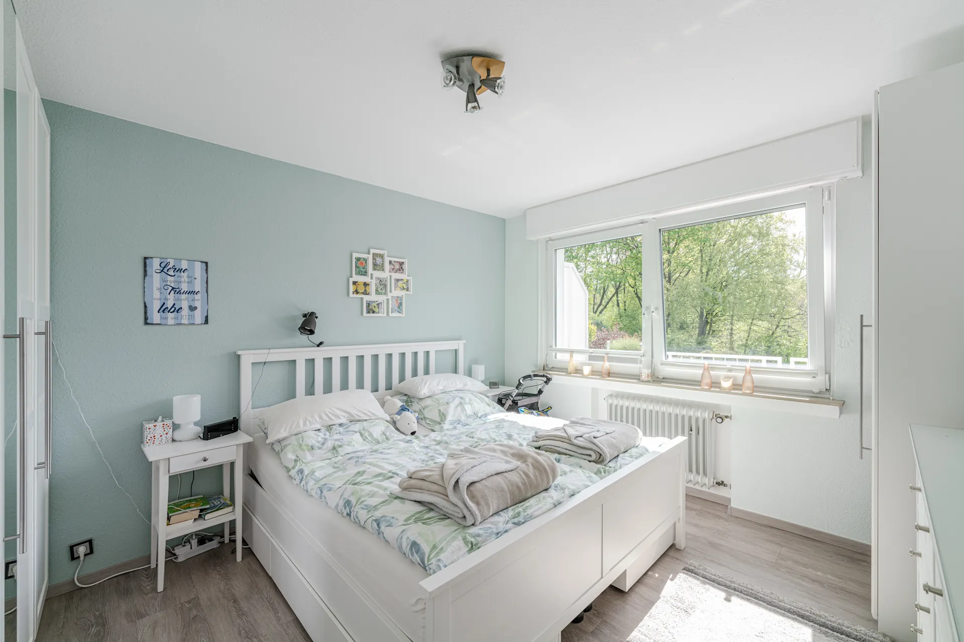 Helles Schlafzimmer mit Doppelbett, Nachttisch, großem Fenster und Blick ins Grüne.