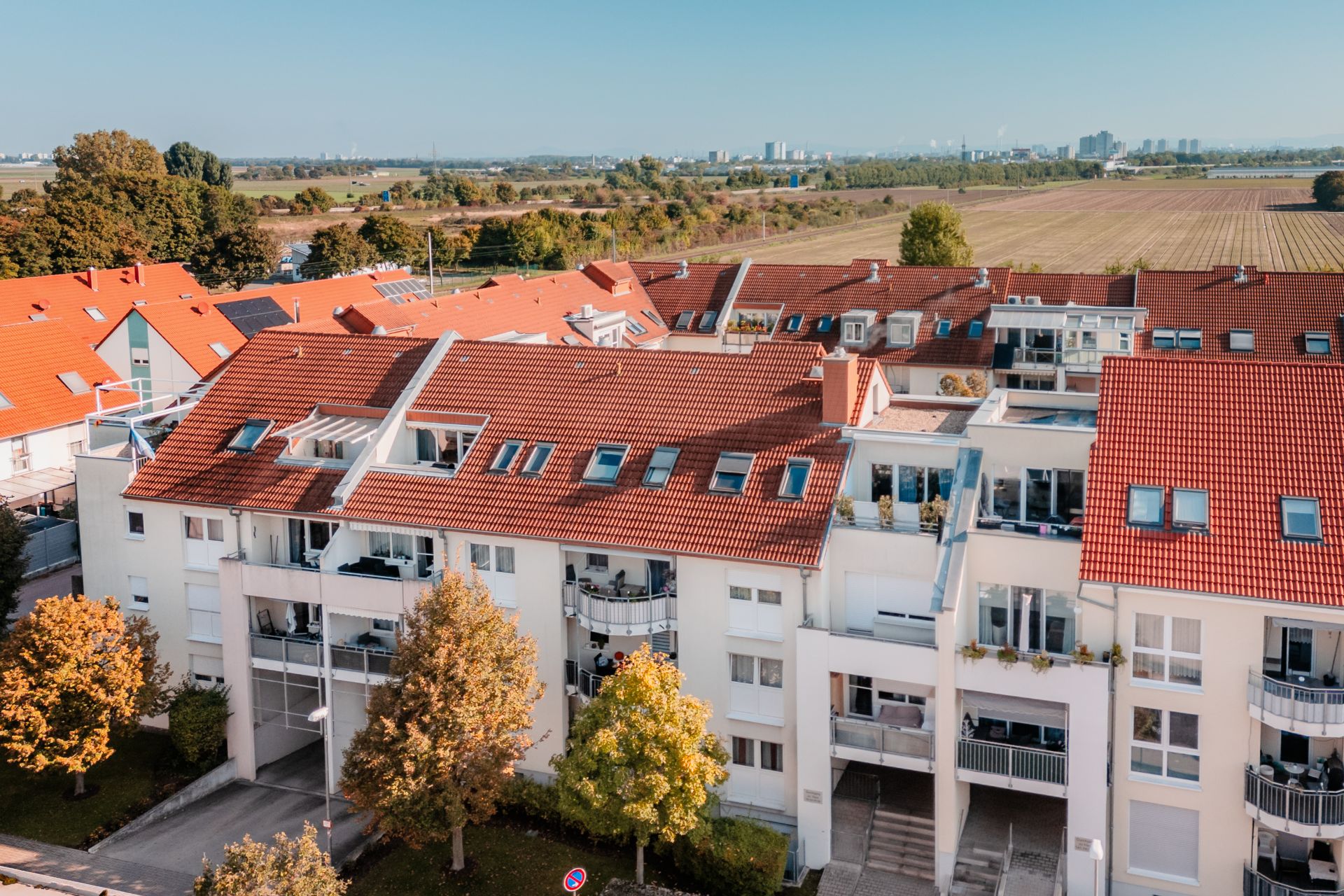Mehrstöckiges Wohnhaus mit roten Dächern, Balkonen und Bäumen davor.