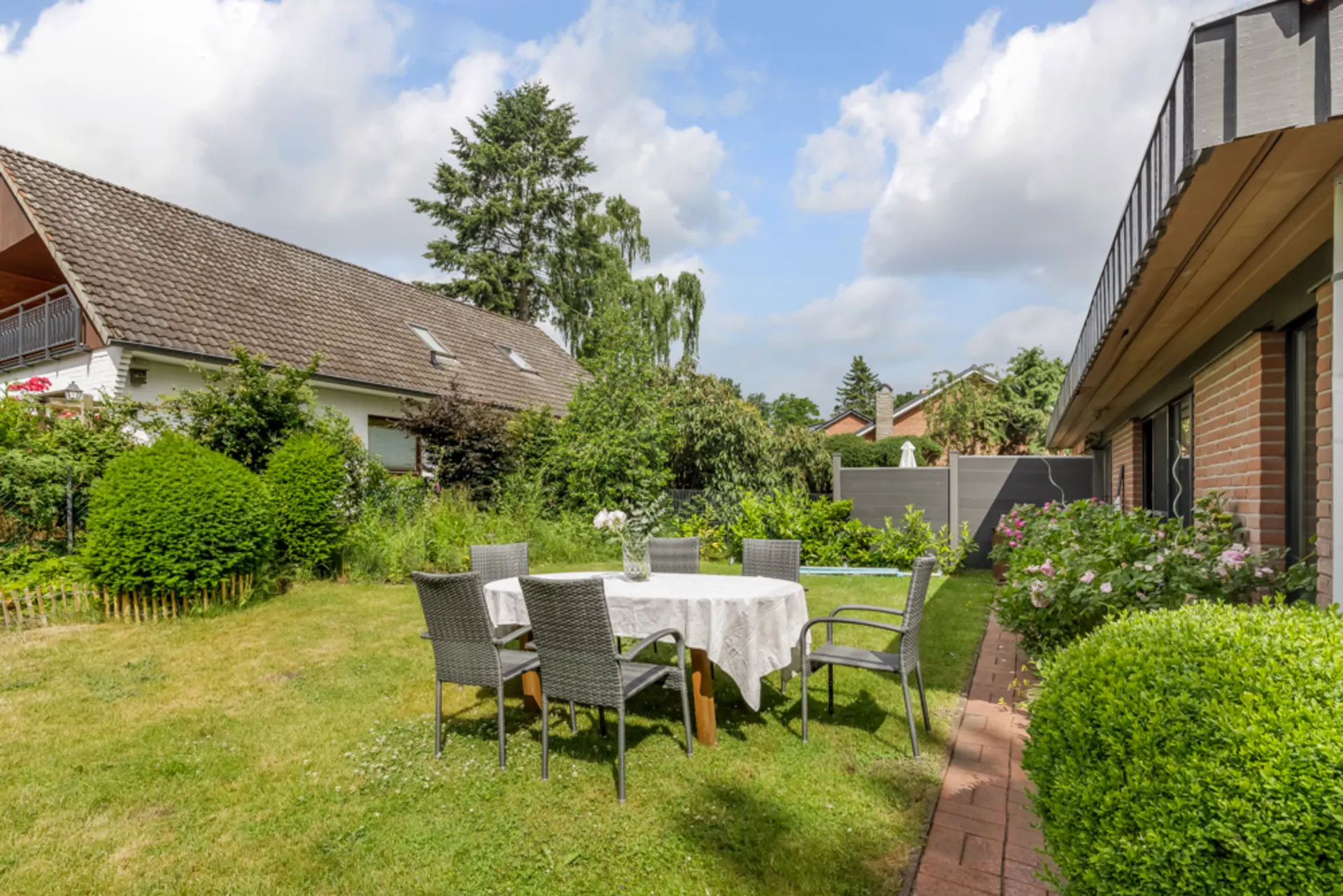 Garten mit Rasen, Gartentisch und vier Stühlen, umgeben von Büschen und Blumen.