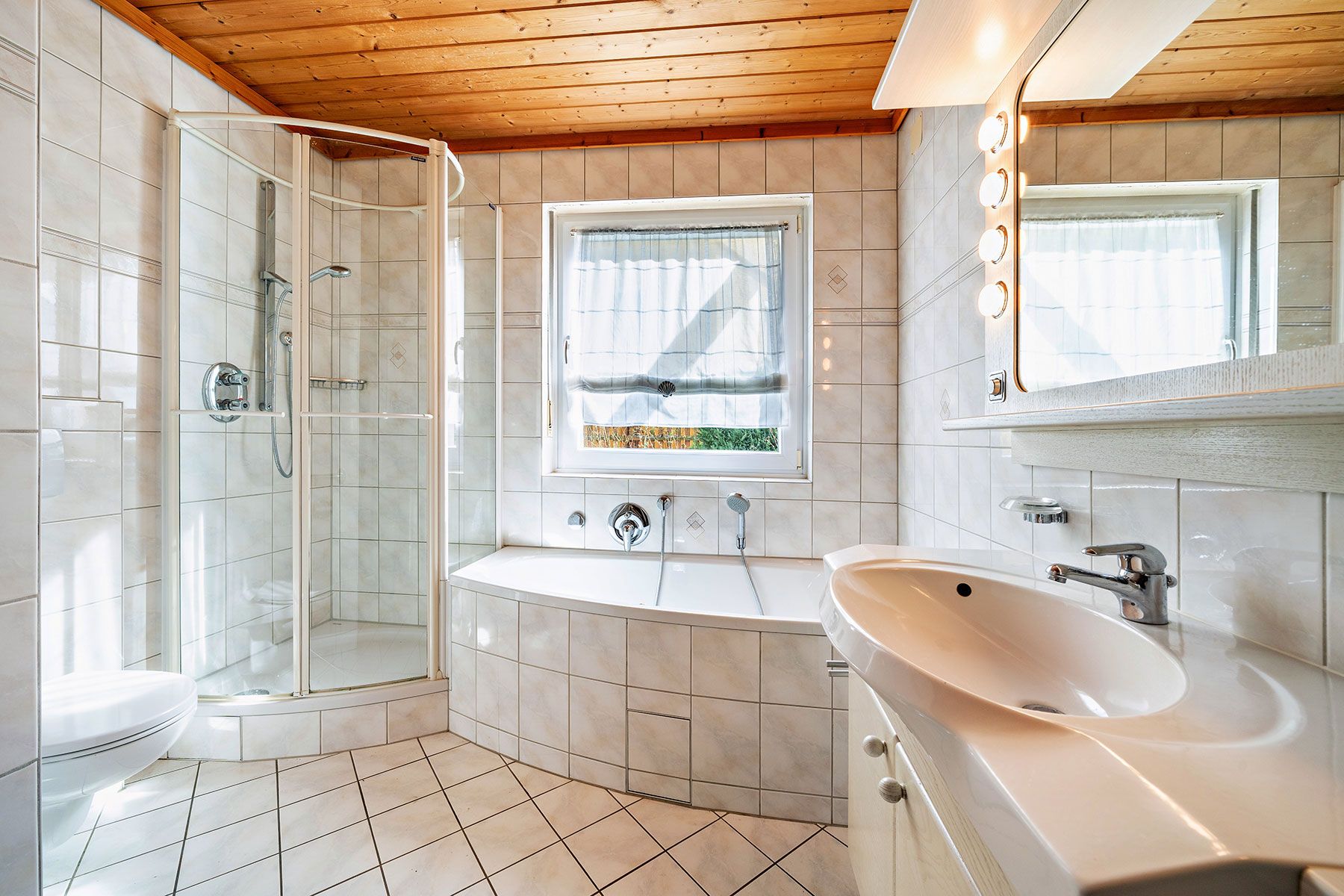 Helles Bad mit Dusche, Badewanne, Waschbecken und großem Fenster, gefliest, Holzdecke.