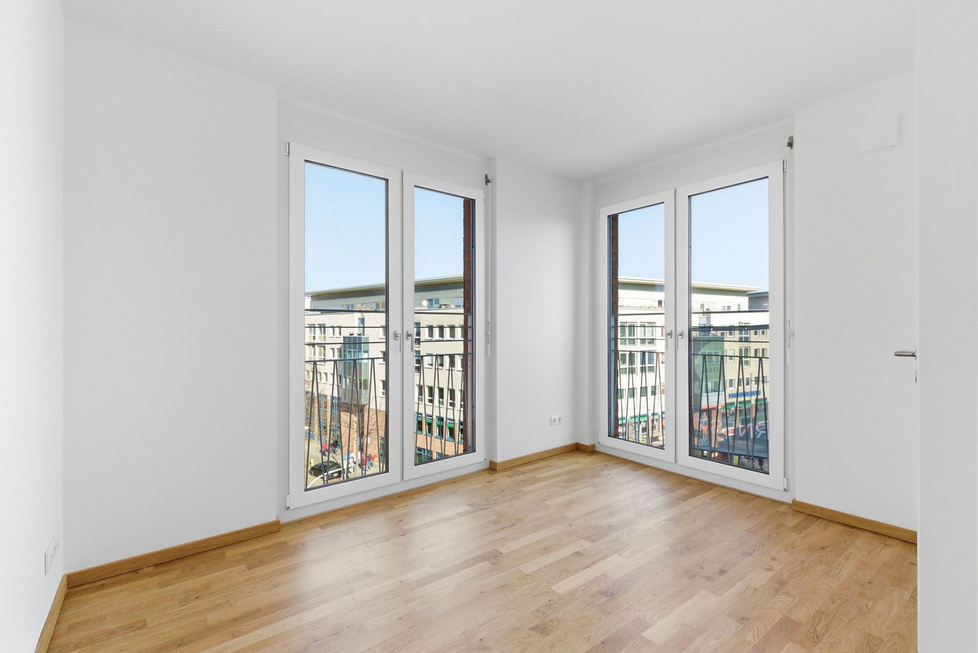 Helles Zimmer mit Parkettboden und zwei großen bodentiefen Fenstern.