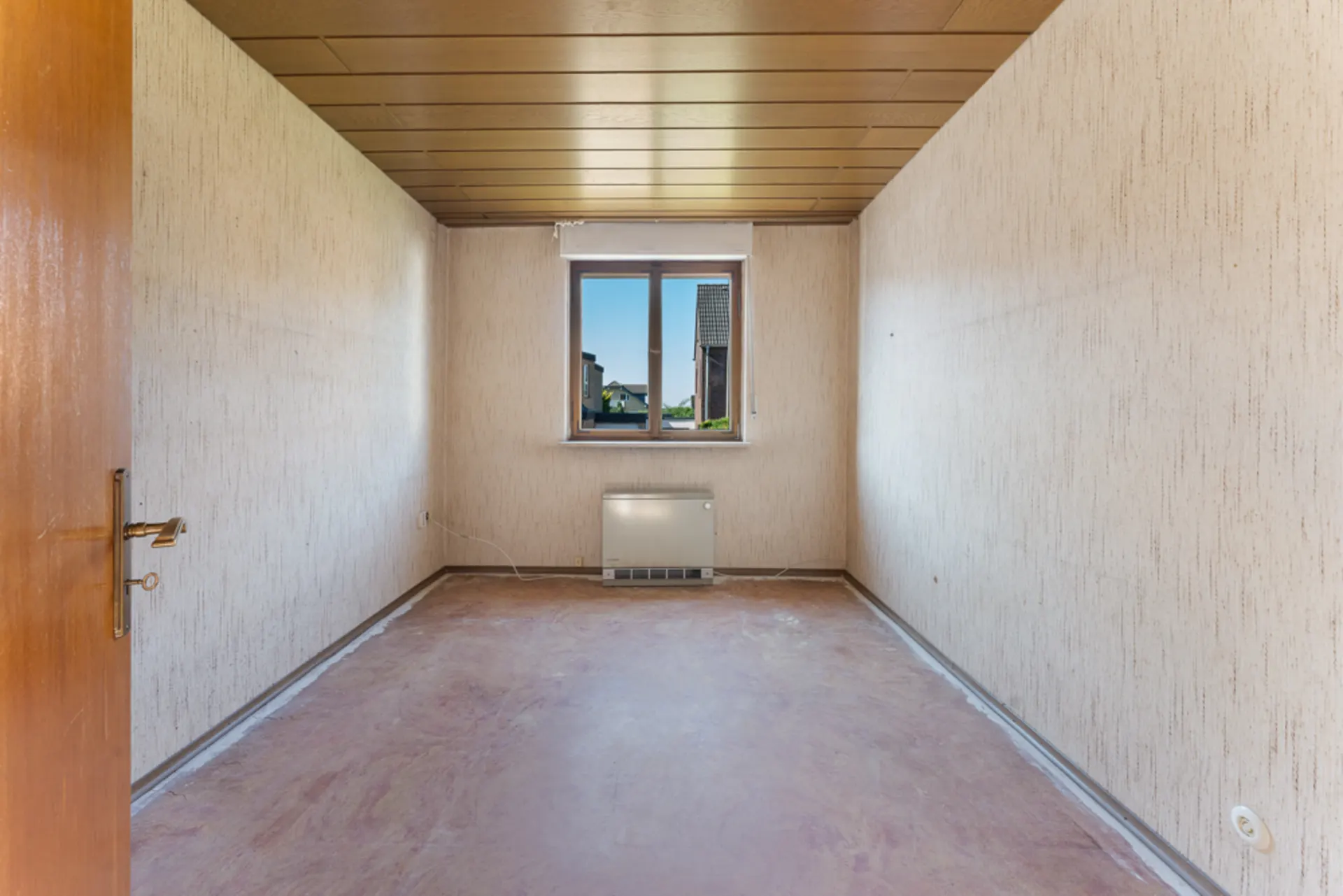 Leerer Raum mit offenem Holztür, Fenster und Heizkörper unter dem Fenster.