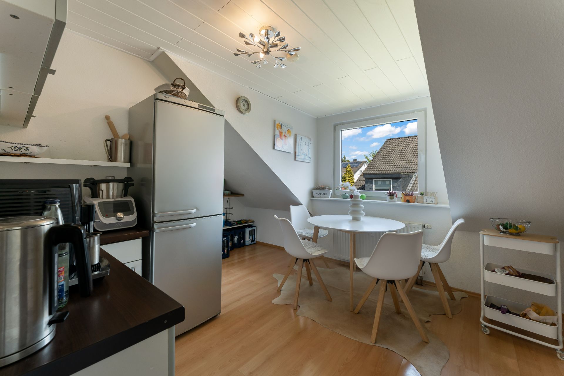 Helle Küche mit Esstisch, vier Stühlen, großem Fenster und Kühlschrank.
