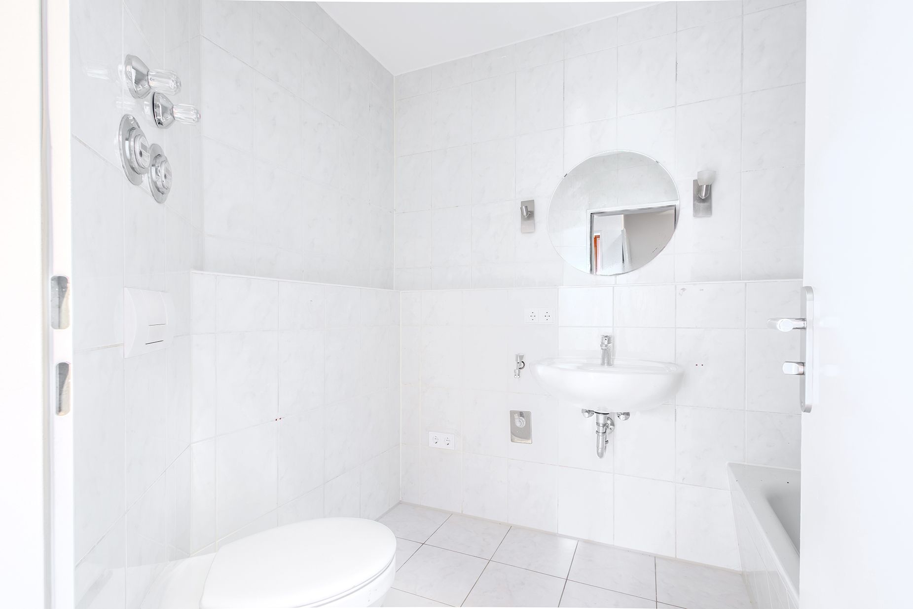 Helles Badezimmer mit WC, Waschbecken, rundem Spiegel und Badewanne.