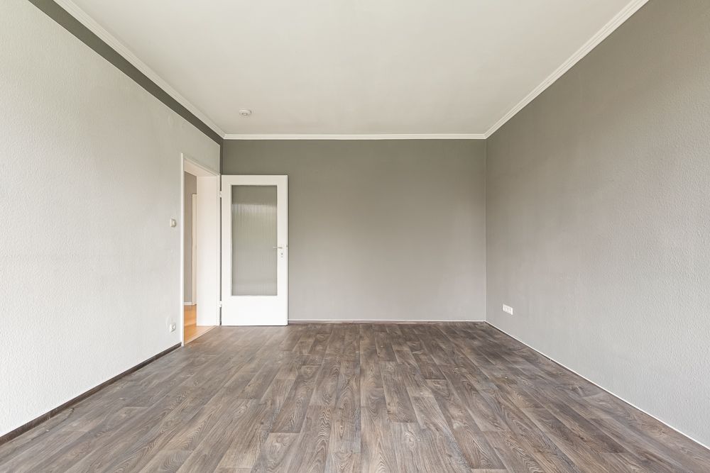 Leerer Raum mit grauen Wänden, weißer Tür und dunklem Holzboden.