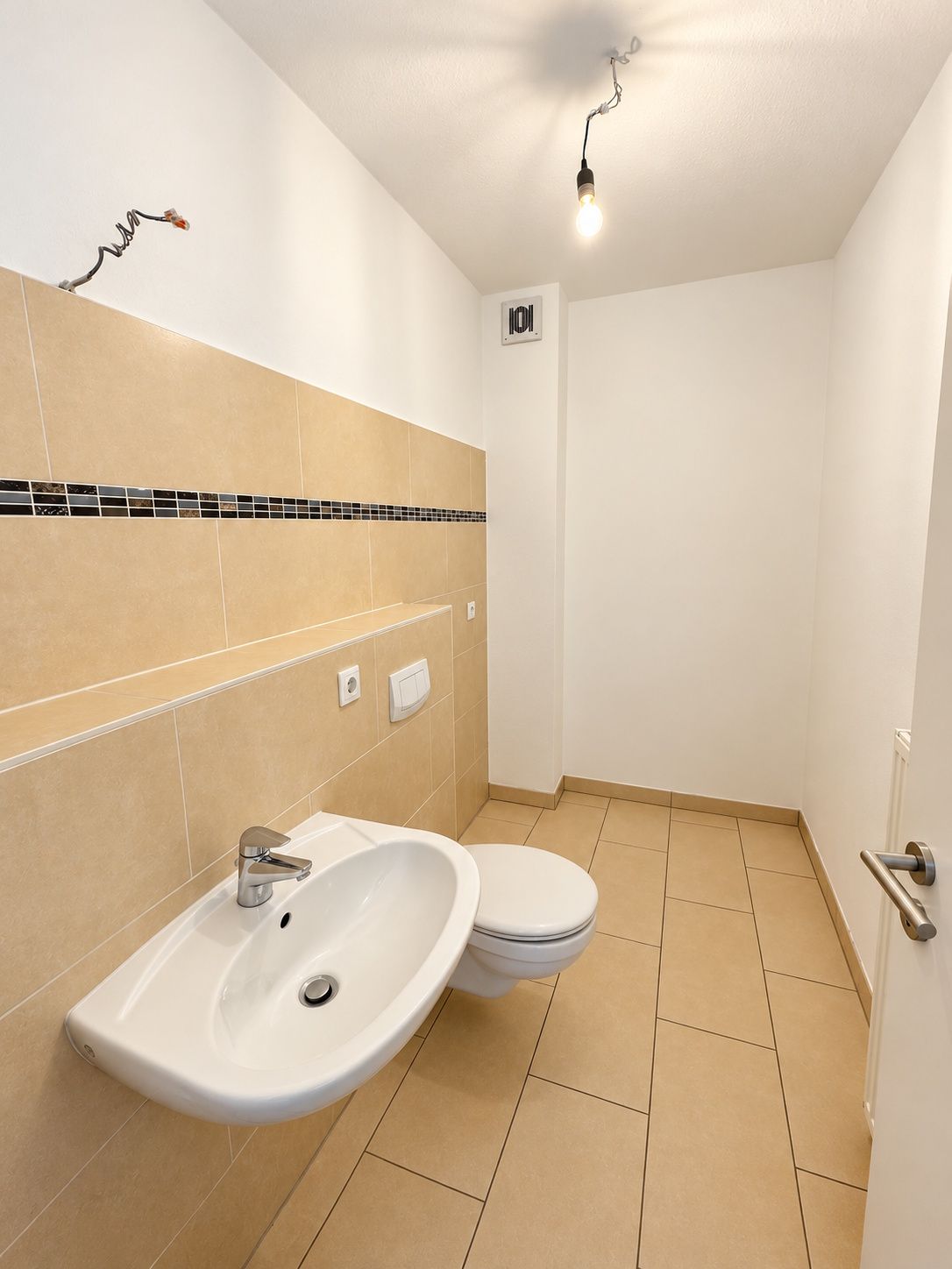 Helles Badezimmer mit Waschbecken, Toilette, beigen Fliesen und einer Glühbirne an der Decke.