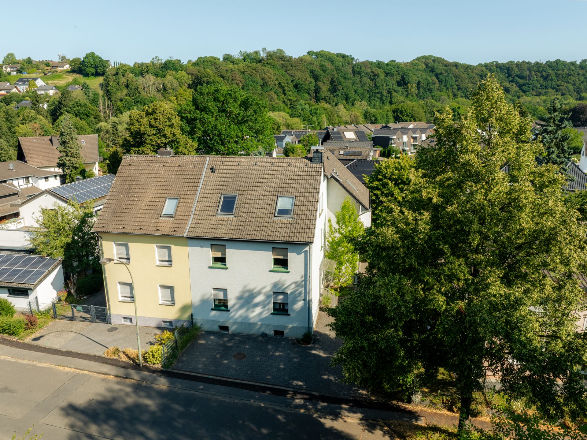 Zweistöckiges Wohnhaus mit Dachfenstern, umgeben von Bäumen und Nachbarhäusern.