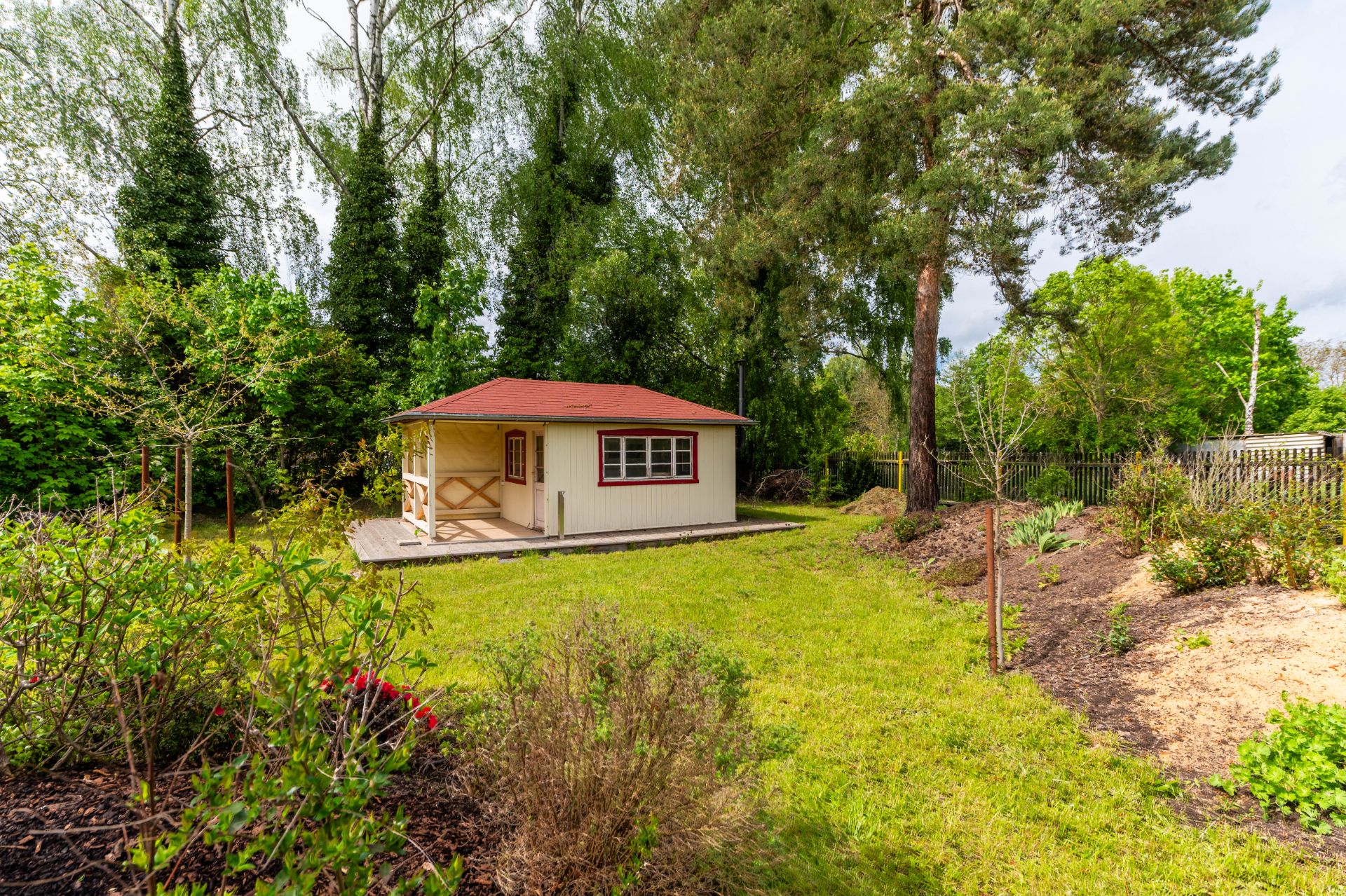 Garten mit kleinem Holzhaus, grünem Rasen und umgebenden Bäumen.