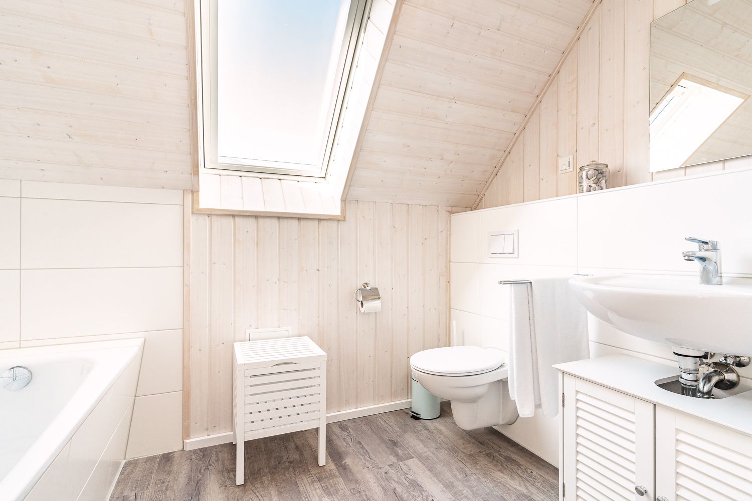 Helles Badezimmer mit Dachfenster, Toilette, Waschbecken, Badewanne und Hocker.