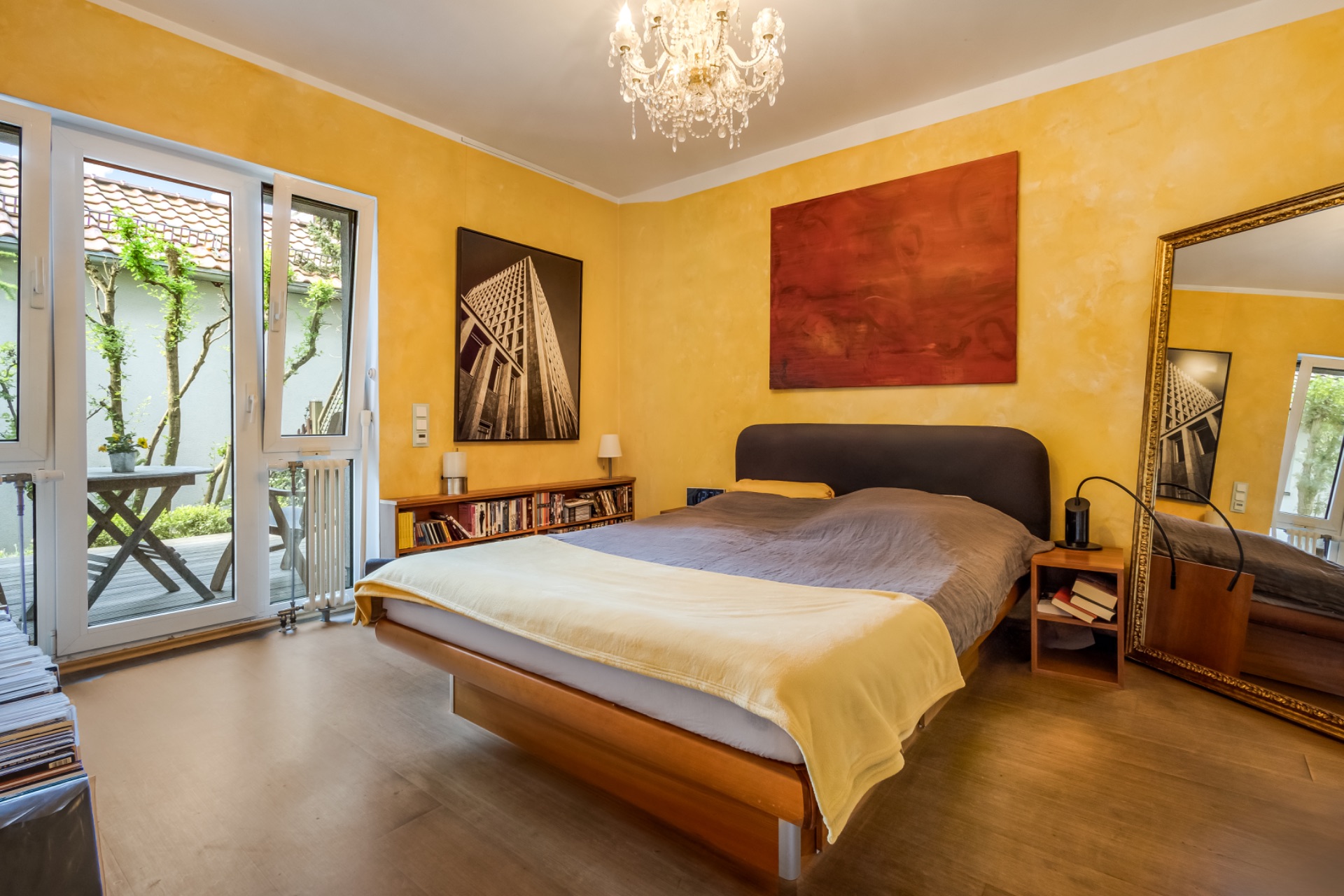 Schlafzimmer mit gelben Wänden, Doppelbett, großem Spiegel und Zugang zu einer Terrasse.