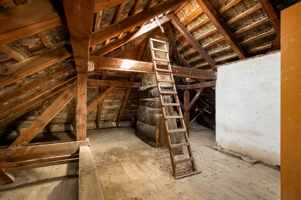 Dachboden mit Holzträgern, einer Holzleiter und sichtbaren Holzbalken.