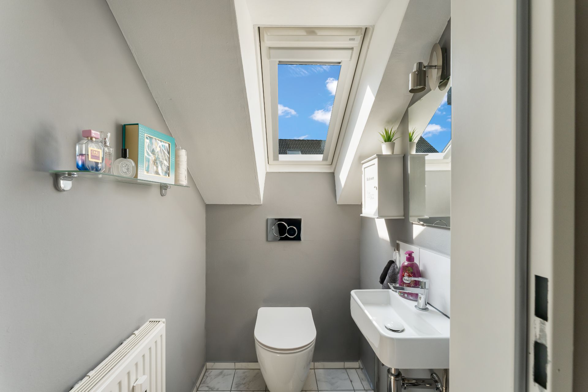 Modernes kleines Bad mit Dachfenster, Toilette, Waschbecken und Spiegel.