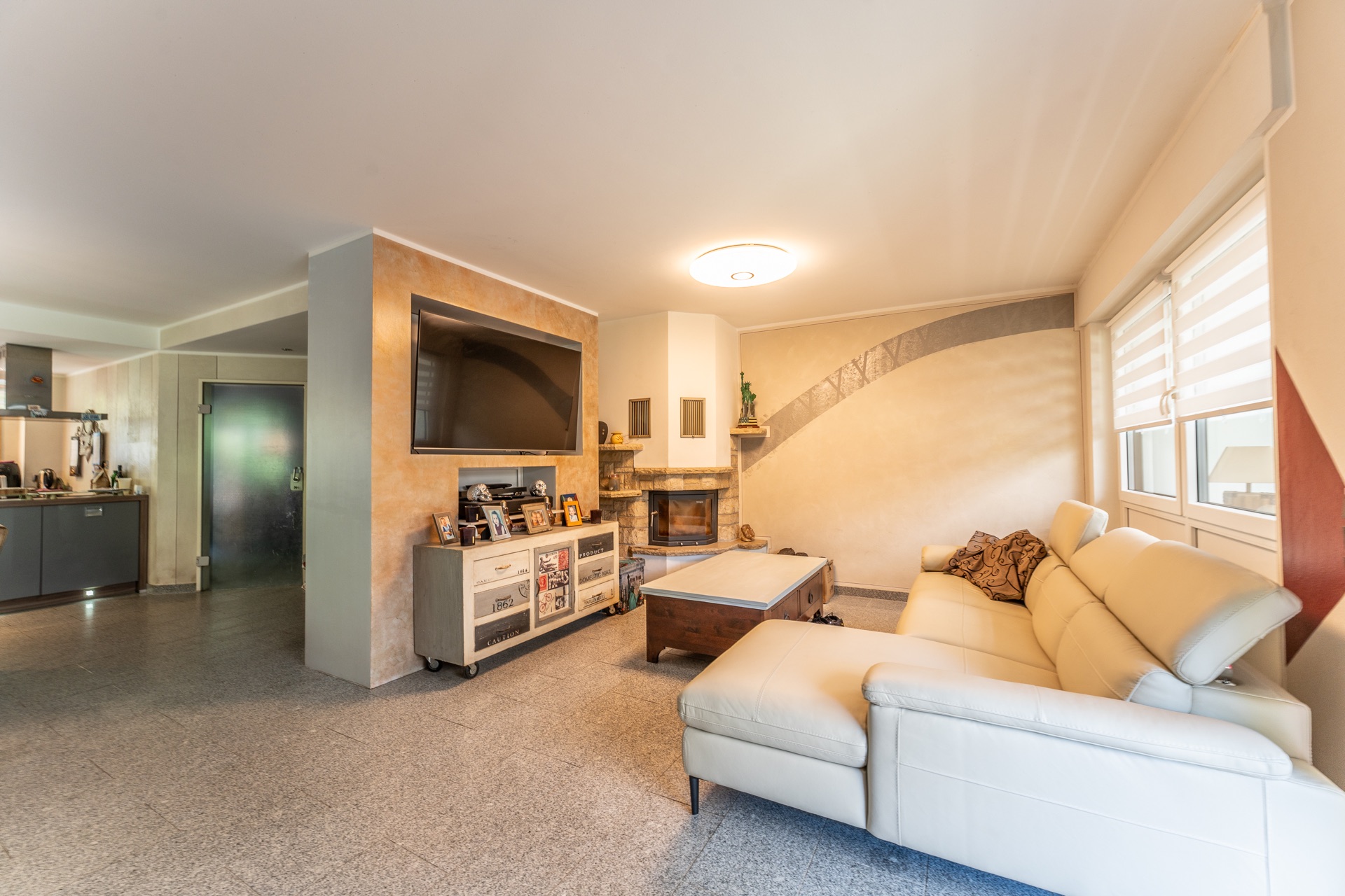 Helles Wohnzimmer mit beiger Eckcouch, Couchtisch, TV an der Wand und Kamin.