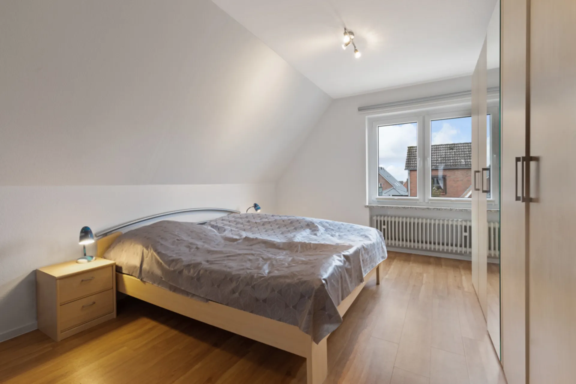 Schlafzimmer mit Doppelbett, Nachttischen, Kleiderschrank und großem Fenster.