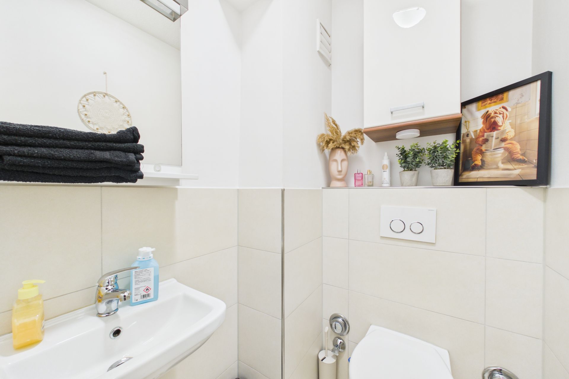 Kleines Bad mit Waschbecken, Toilette, Handtüchern, Dekoration und einem Bild an der Wand.