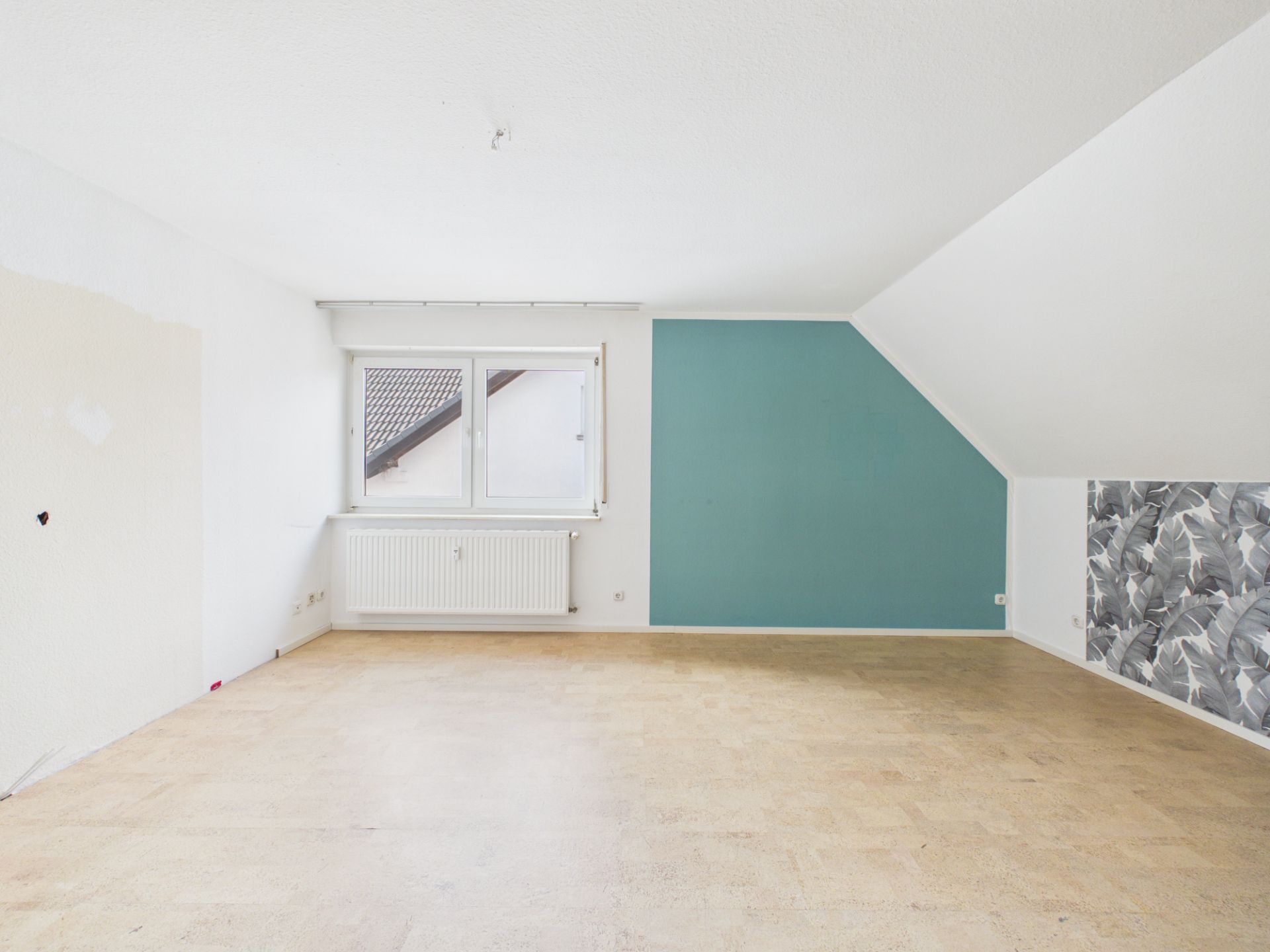 Leerer Raum mit Fenster, Heizkörper und unterschiedlich farbigen Wänden.