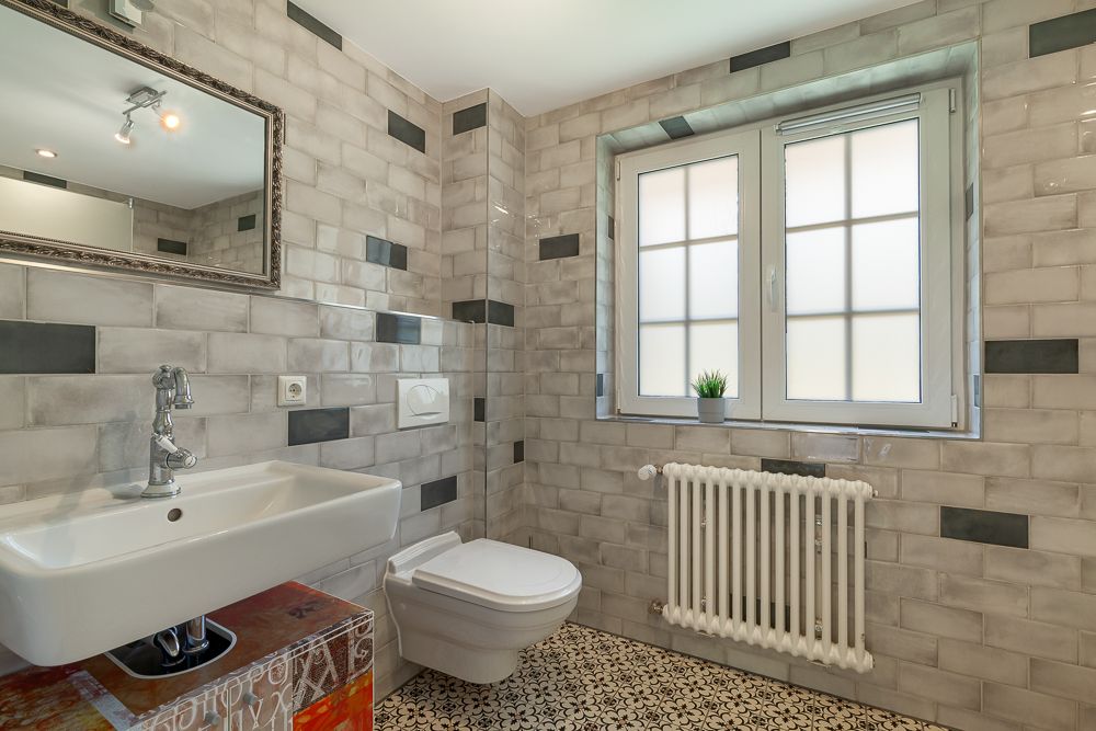 Modernes Badezimmer mit Wandfliesen, Waschbecken, Spiegel, Toilette und Fenster mit Heizung.