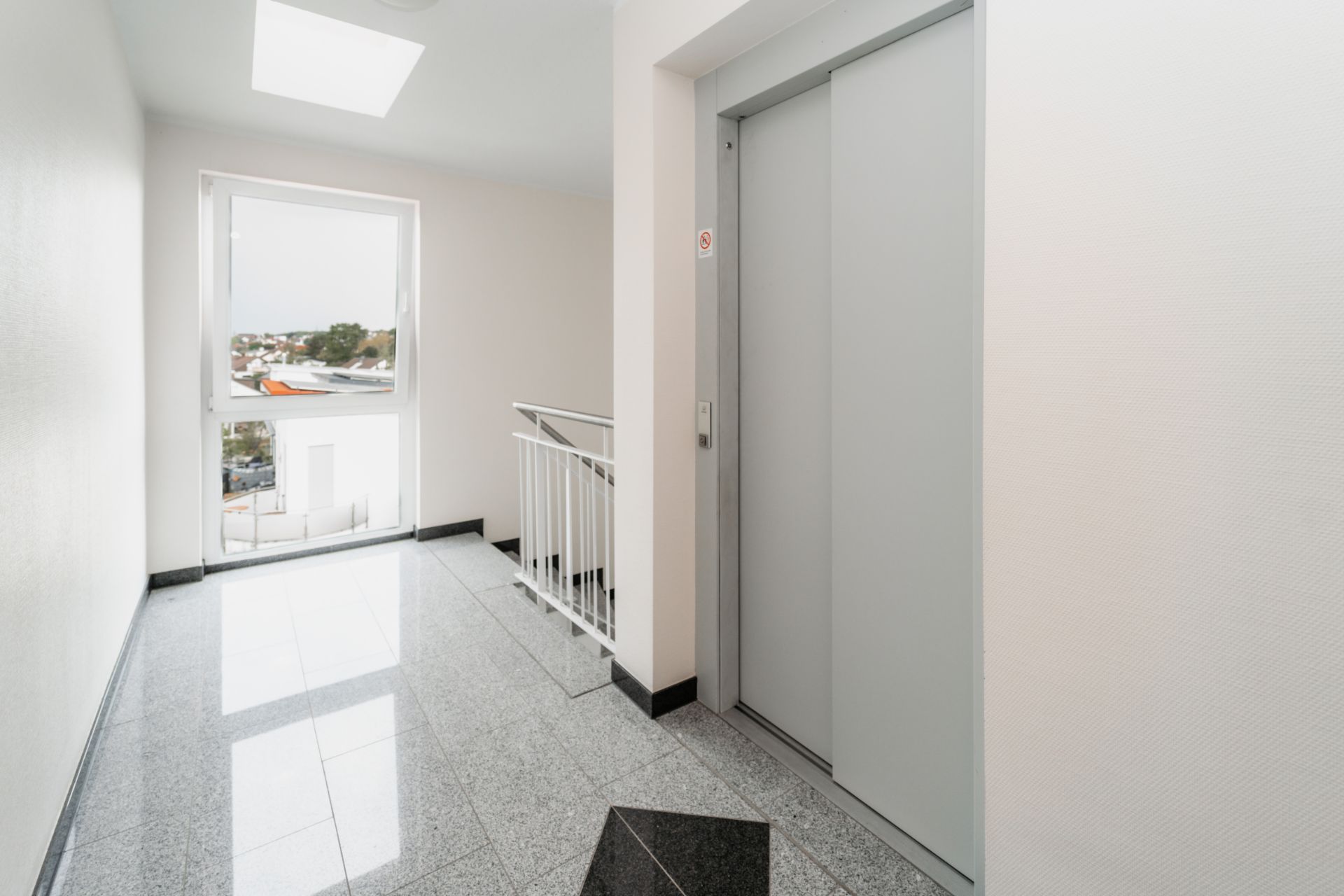 Heller Flur mit Fenster, Aufzugstür und Treppengeländer in einem Wohngebäude.