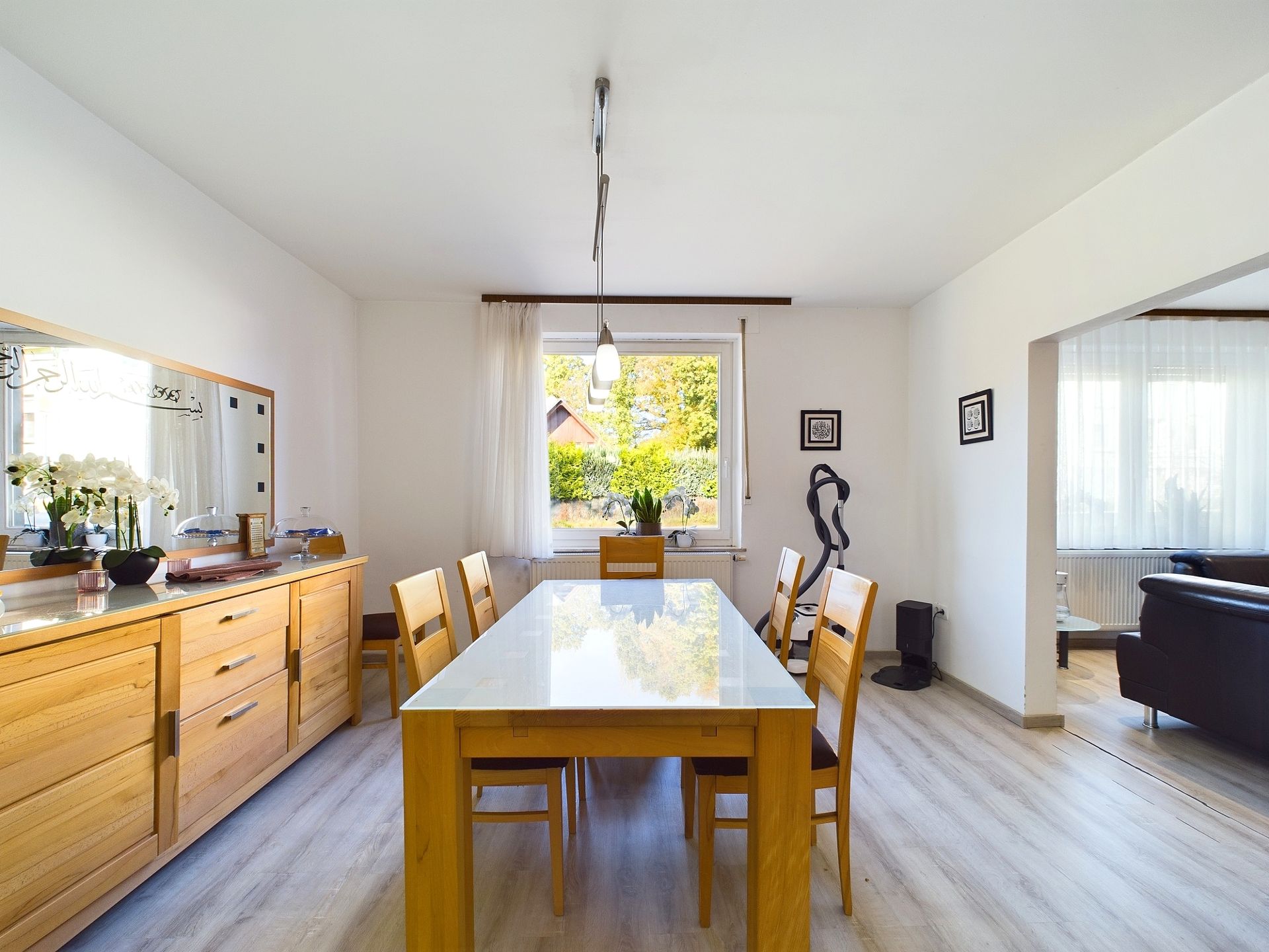 Helles Esszimmer mit Holztisch, sechs Stühlen, Sideboard und Fenster mit Blick nach draußen.