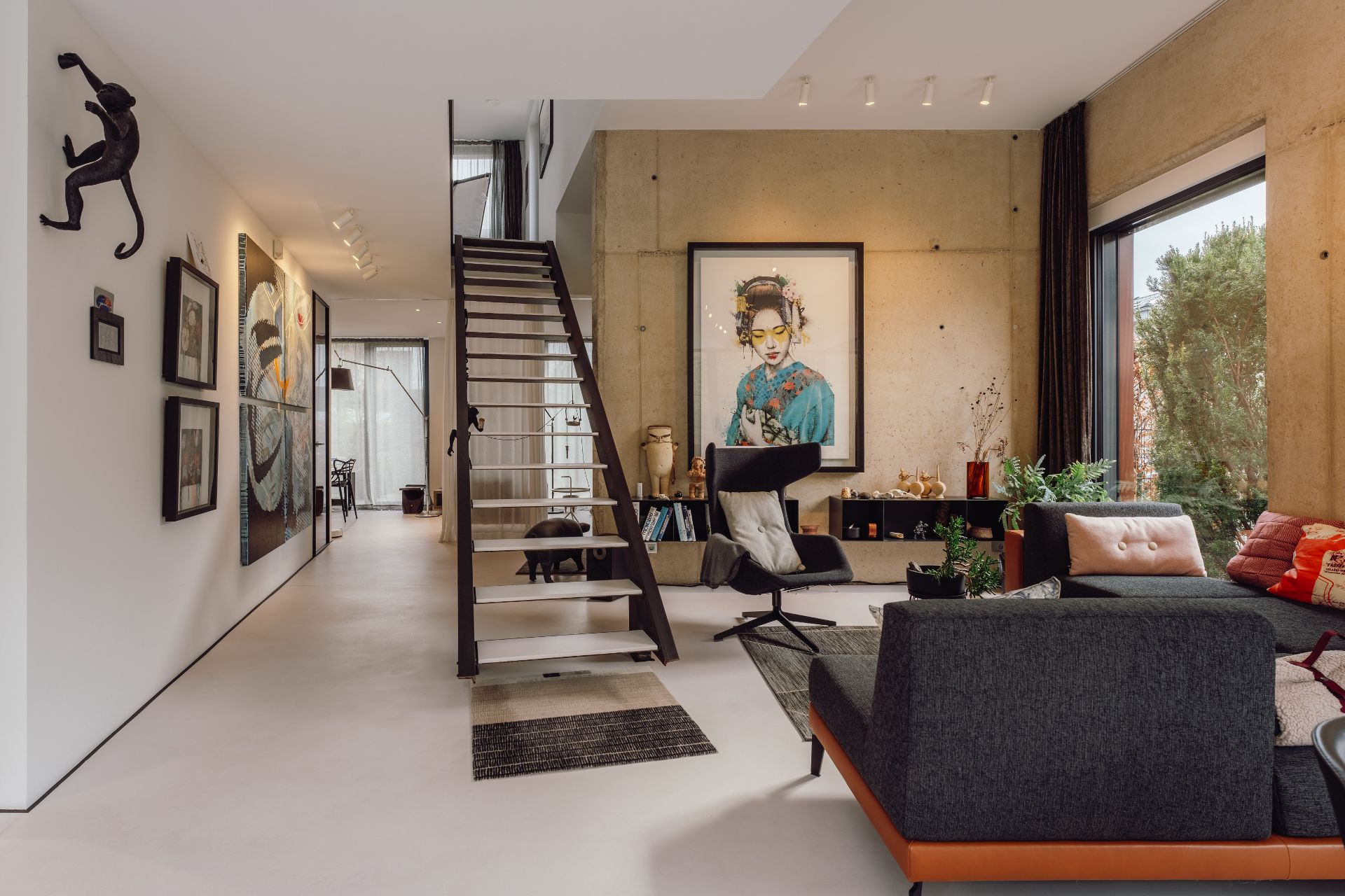 Modernes Wohnzimmer mit Treppe, Kunstwerken an den Wänden und großen Fenstern.
