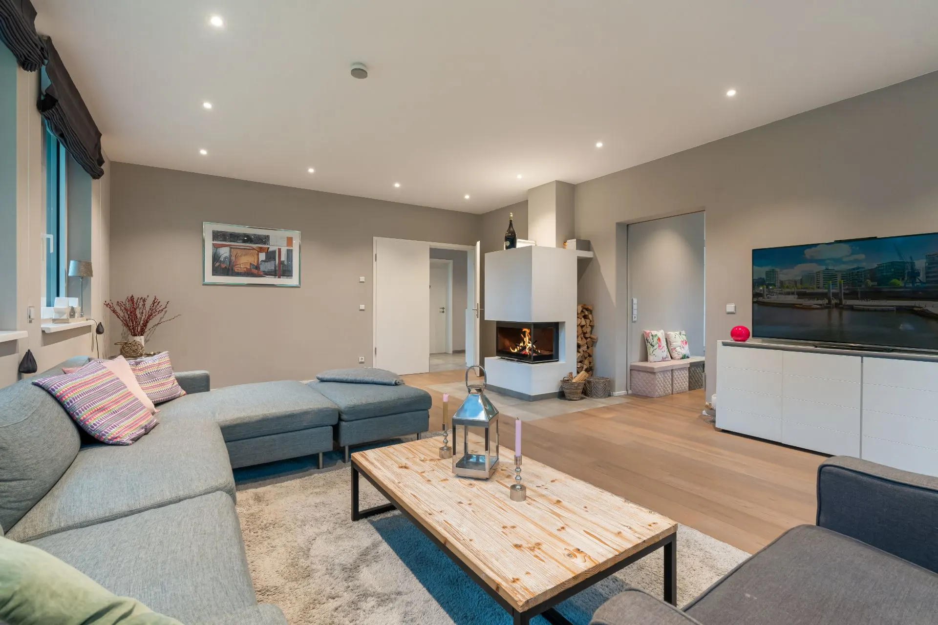Modernes Wohnzimmer mit grauer Eckcouch, Couchtisch, Fernseher und Kamin.
